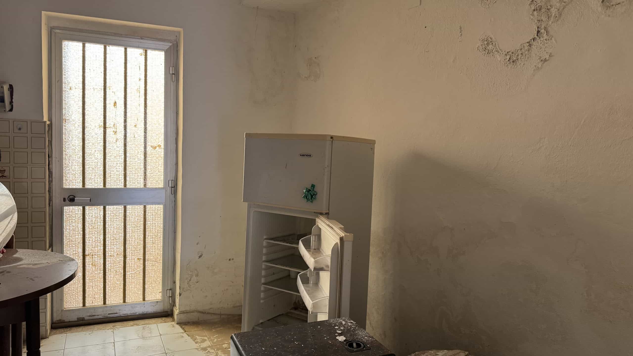 Serratura di sicurezza sulla porta d'ingresso di una casa abbandonata con pareti danneggiate e muffa, ambiente interno trascurato e poco illuminato.