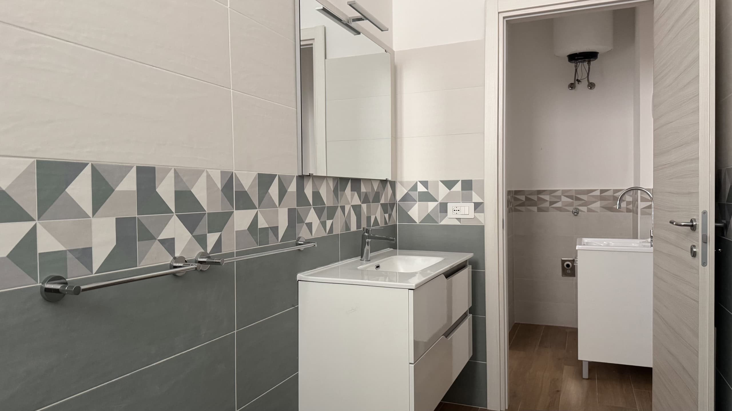Lavabo e bagno moderno con piastrelle geometriche in tonalità neutre, arredo minimalista e specchio grande, ideale per ambienti di design e funzionalità.
