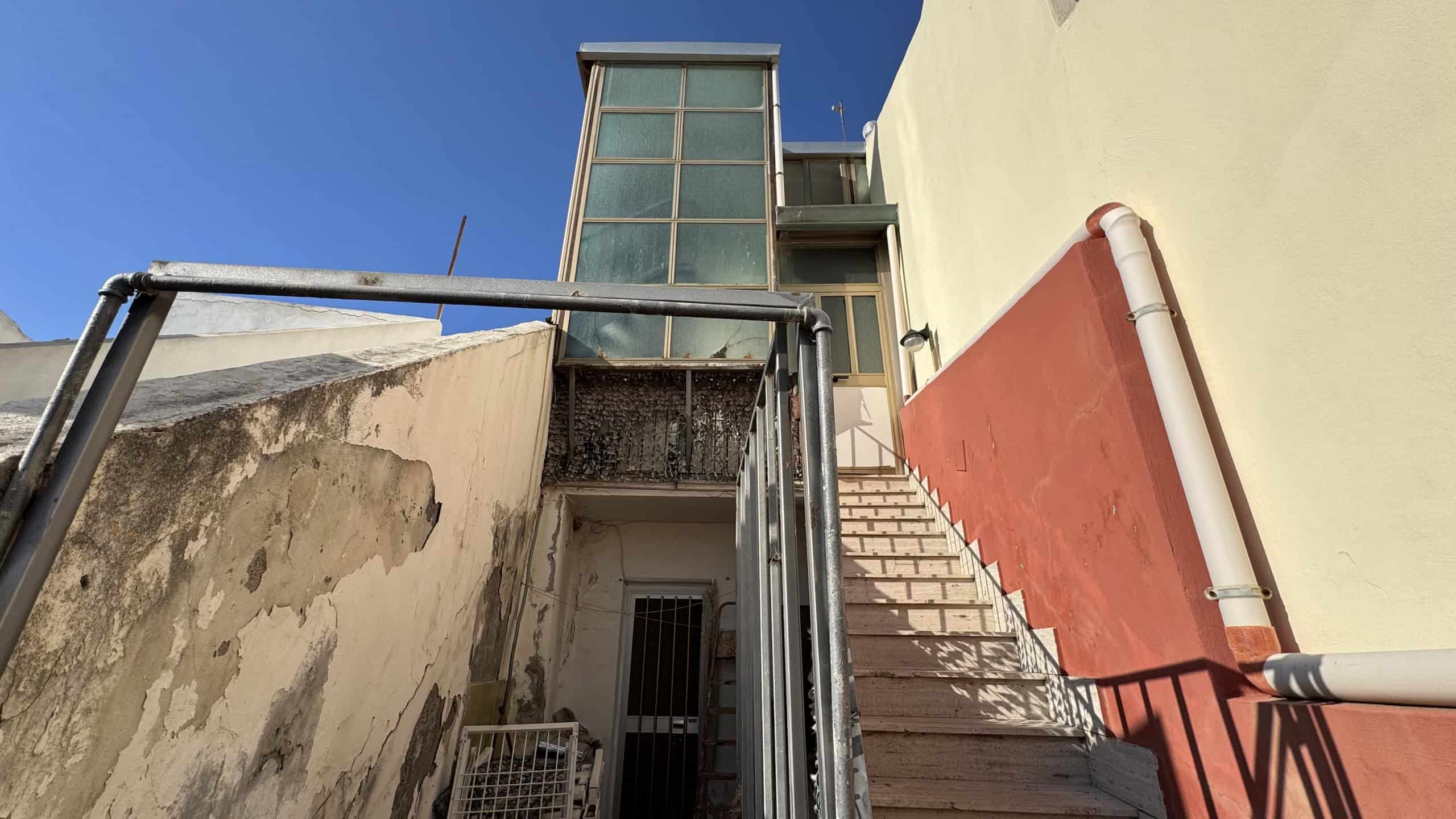 Escalator esterno in un edificio moderno con pareti colorate e struttura in metallo, situato in un'area urbana con cielo sereno. Ideale per immobili residenziali o commerciali innovativi.