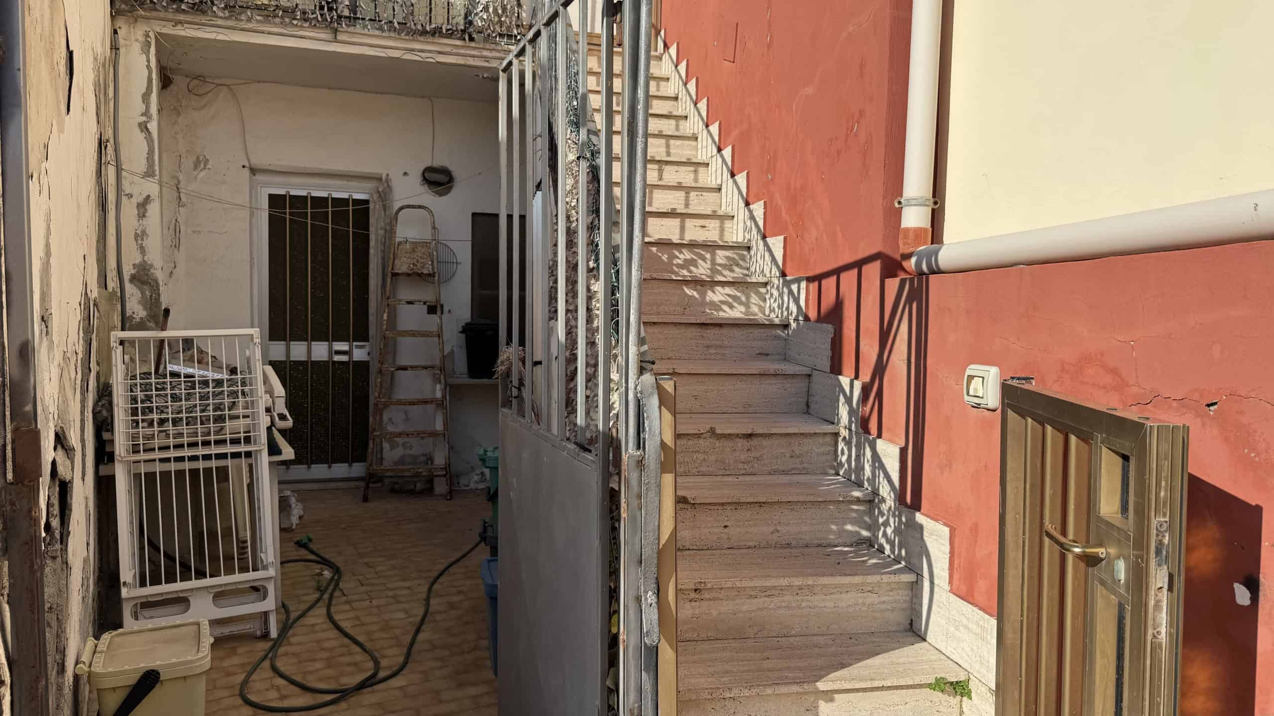 Scalinata esterna in cemento con ringhiera in metallo, situata tra edifici residenziali con pareti colorate, in un cortile urbano.