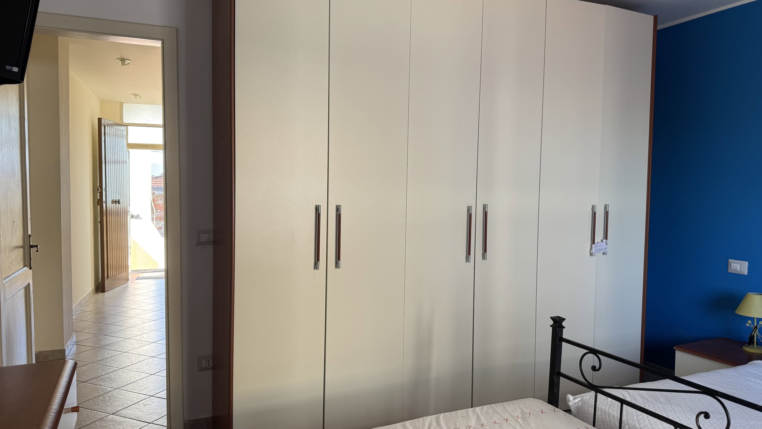 Armadio a muro spazioso con ante lisce in una camera da letto, ideale per ottimizzare lo spazio e organizzare gli abiti. Design semplice e funzionale, perfetto per arredamenti contemporanei.