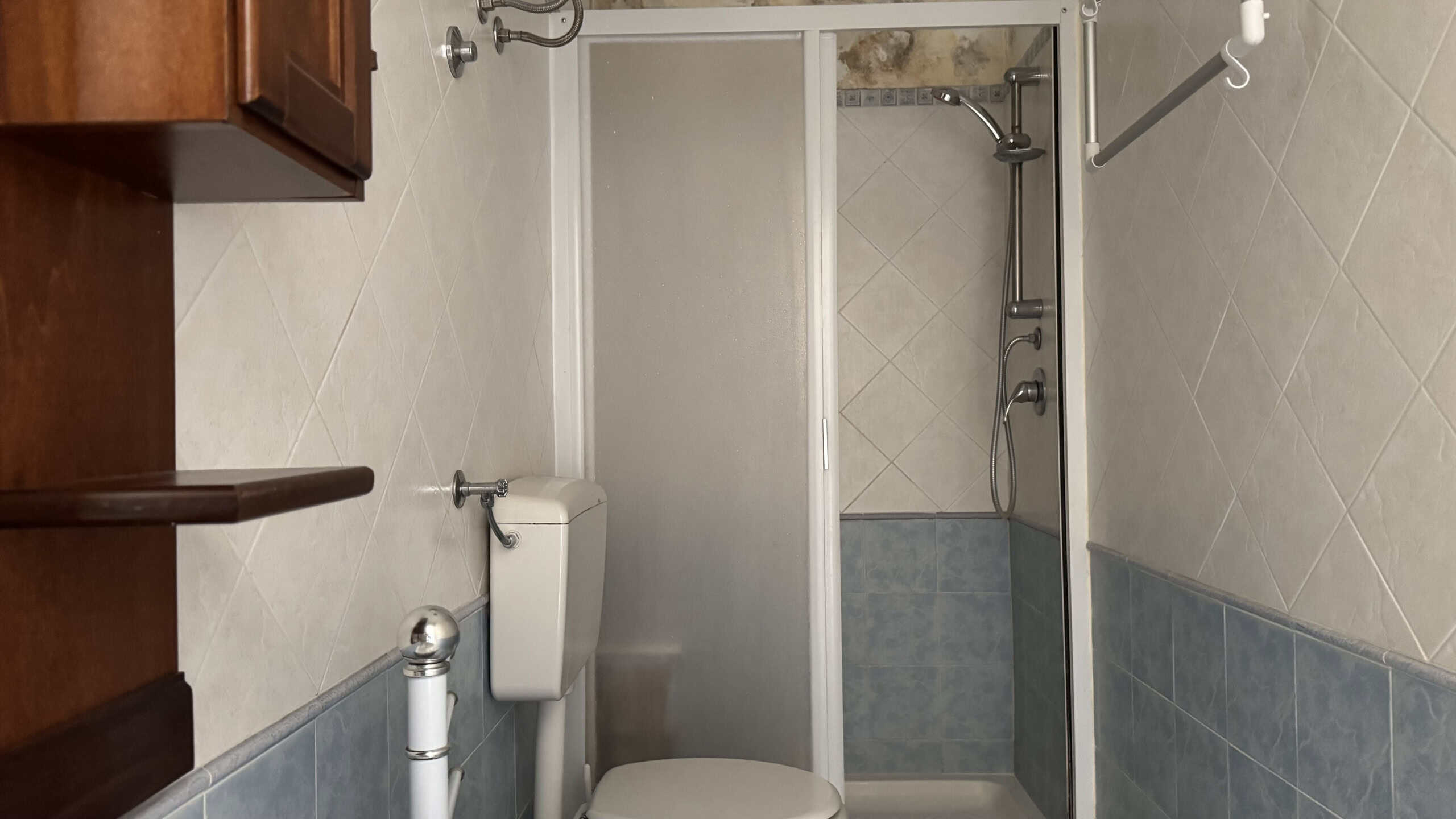 Bagno con doccia, sanitari e piastrelle beige e azzurre, arredamento funzionale e pulito, ideale per ambienti di comfort e praticità.