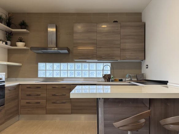 Cucina moderna con mobili in legno chiaro, piani in marmo e pareti bianche, con elettrodomestici e mensole decorative.