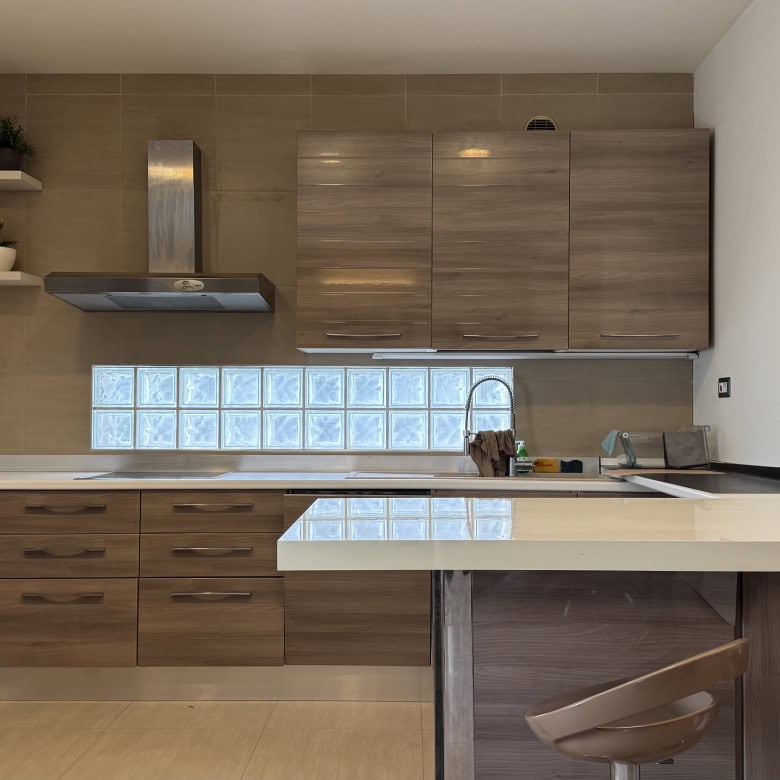 Cucina moderna con mobili in legno chiaro, piani in marmo e pareti bianche, con elettrodomestici e mensole decorative.