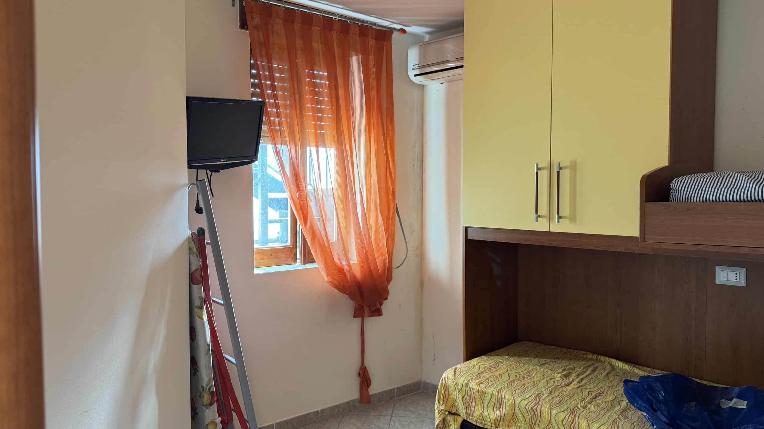 Interno di una stanza moderna con letto a soppalco, aria condizionata e finestra con tende arancioni, ideale per appartamenti di design e comfort.