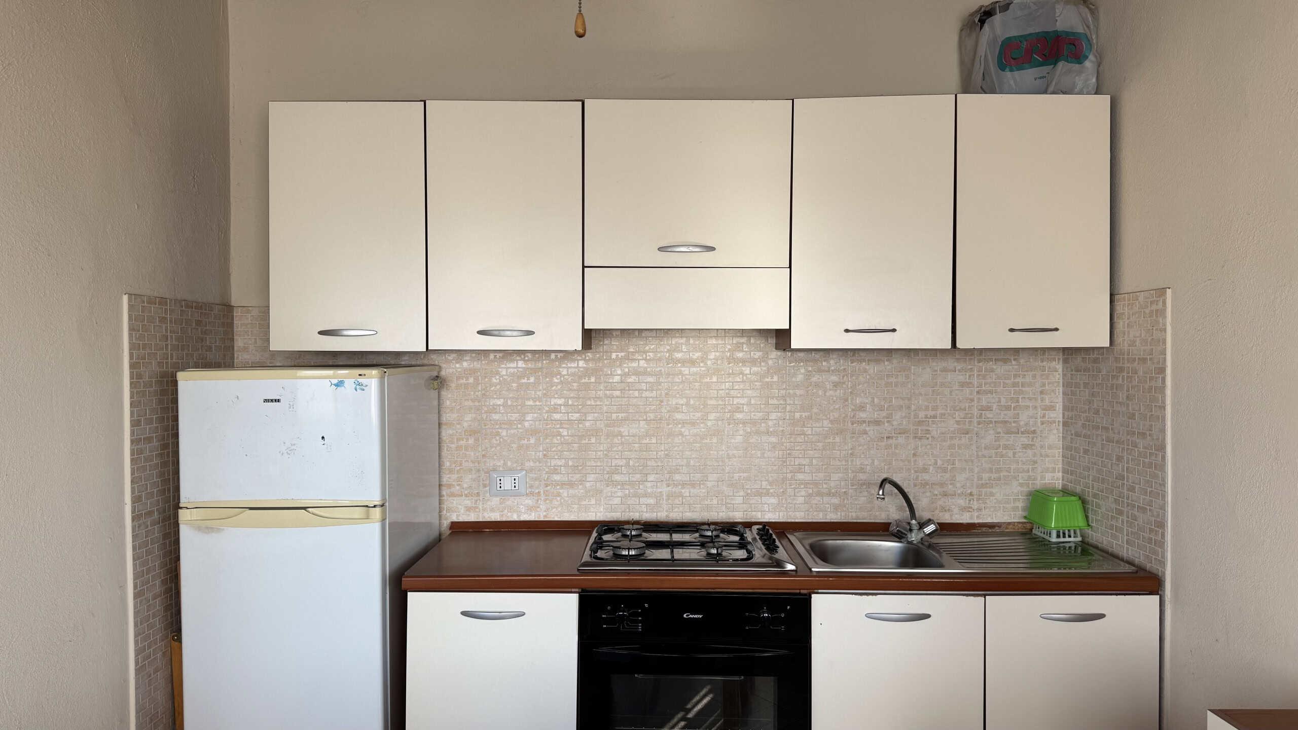 Cucina moderna con frigorifero, piano cottura e lavello in uno spazio compatto, ideale per appartamenti piccoli o monolocali.