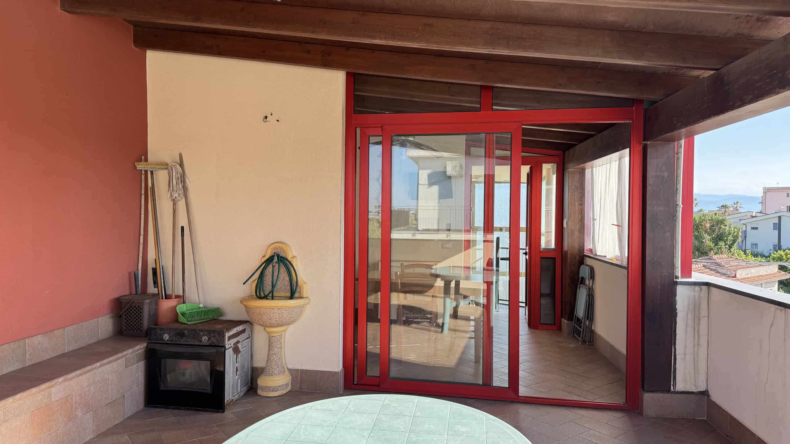Balcone con porta scorrevole in vetro rosso, spazio esterno con vista panoramica, arredi funzionali e decorativi, ideale per relax e convivialità all'aperto.