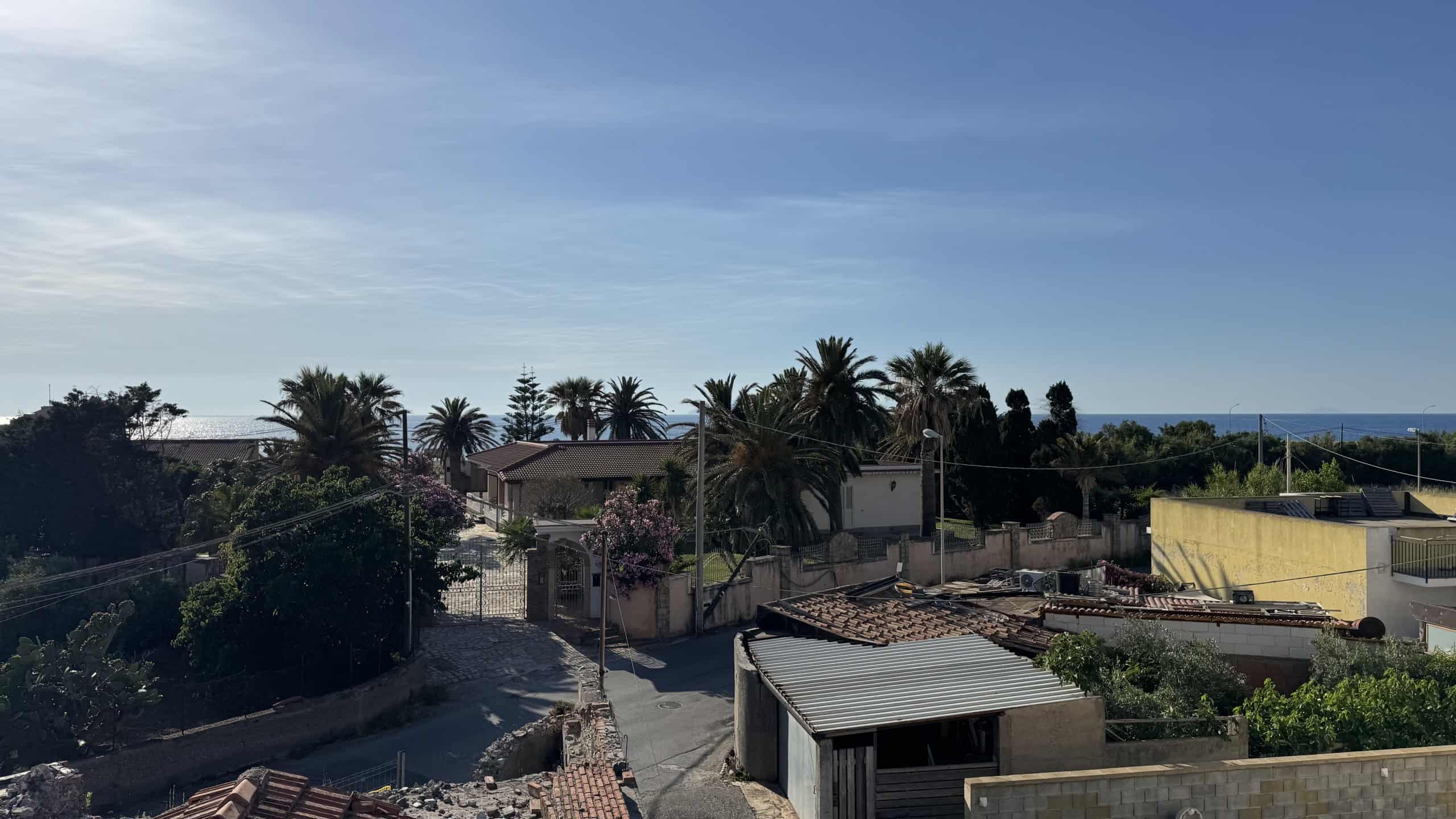 Panorama di ville e case residenziali con palme lungo la costa, vista sul mare in lontananza, cielo sereno, ambiente tranquillo e suggestivo ideale per immobili di lusso.