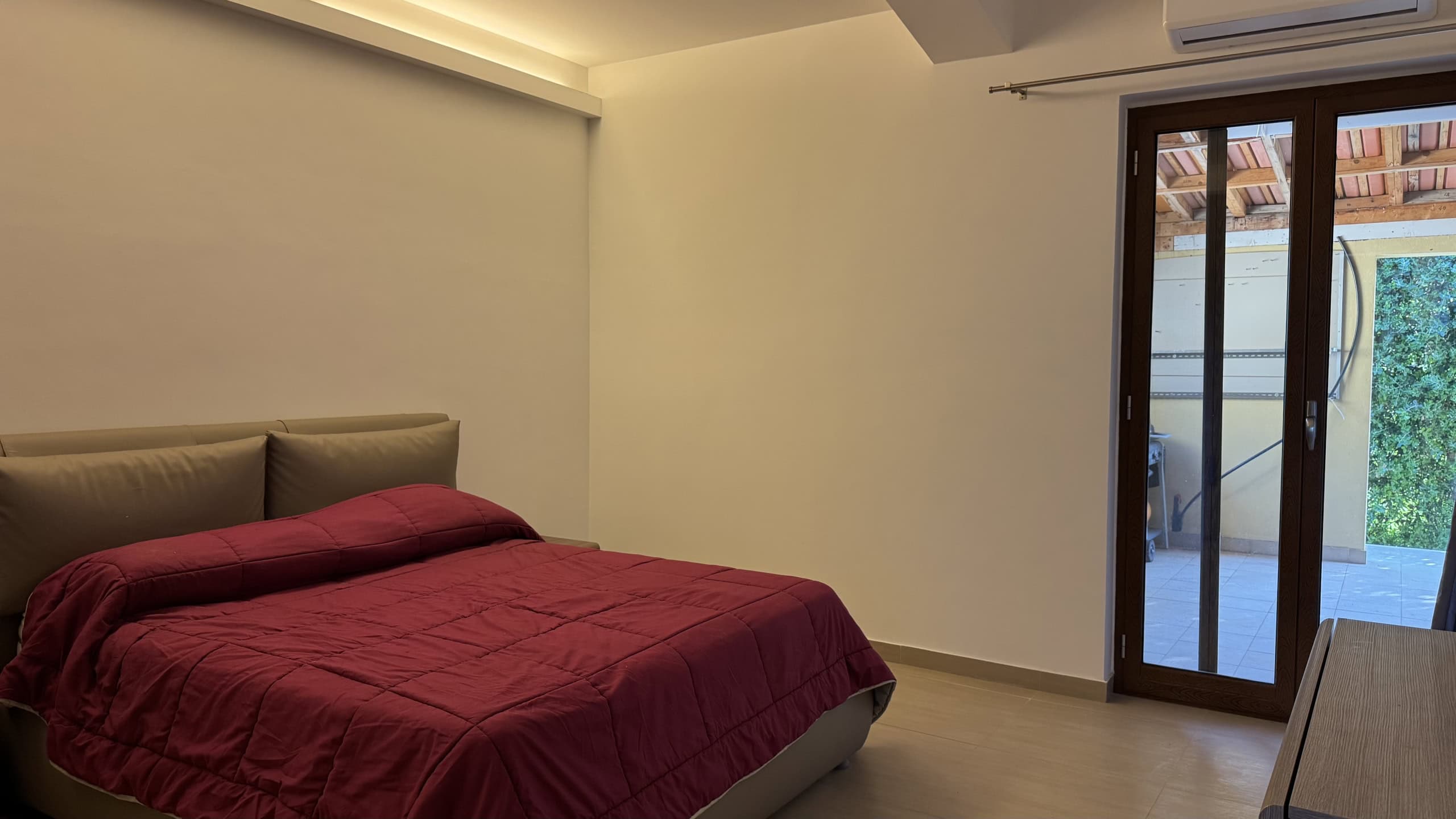 Interno di una camera da letto moderna con letto matrimoniale e accesso a un giardino esterno.