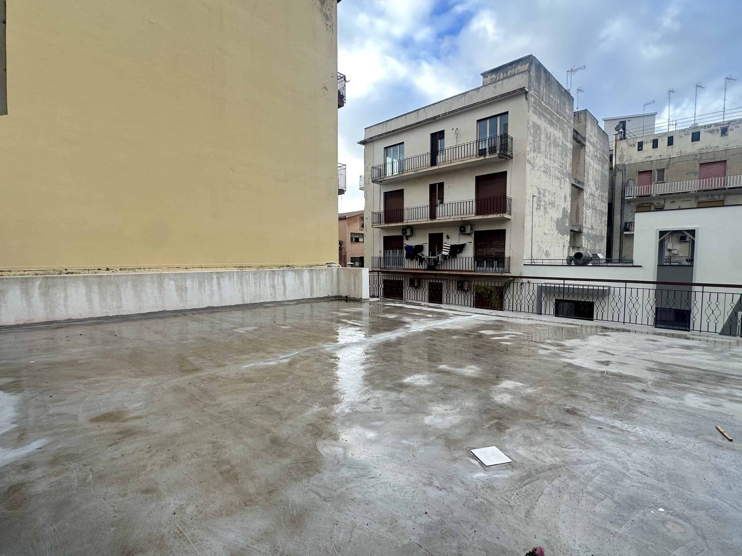 Terrazza urbana con vista su edifici residenziali, pavimento in cemento e cielo nuvoloso, ideale per relax e socializzazione all'aperto.
