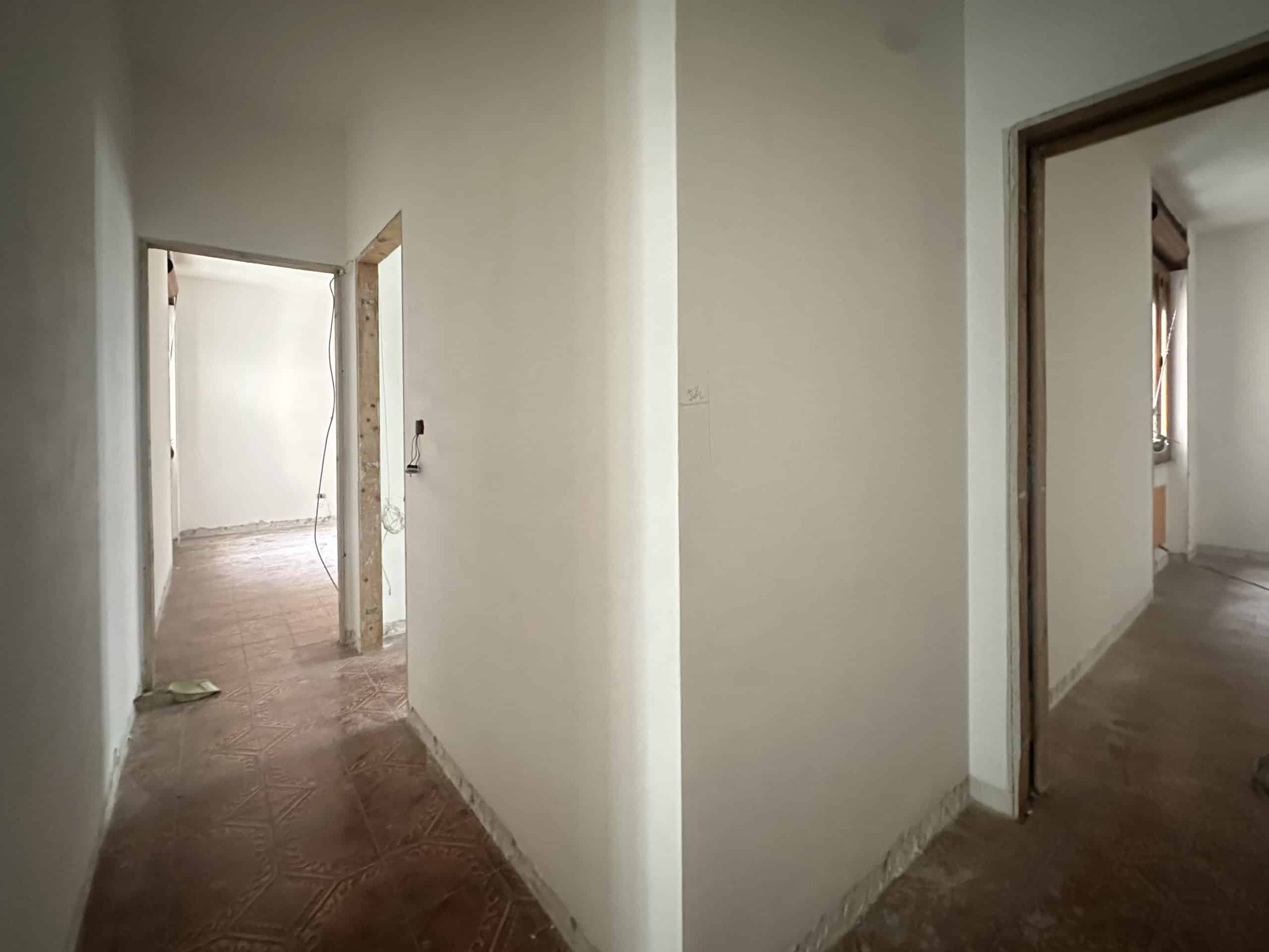 Immagine di un corridoio interno di un appartamento in vendita, con pareti bianche e pavimento in piastrelle.