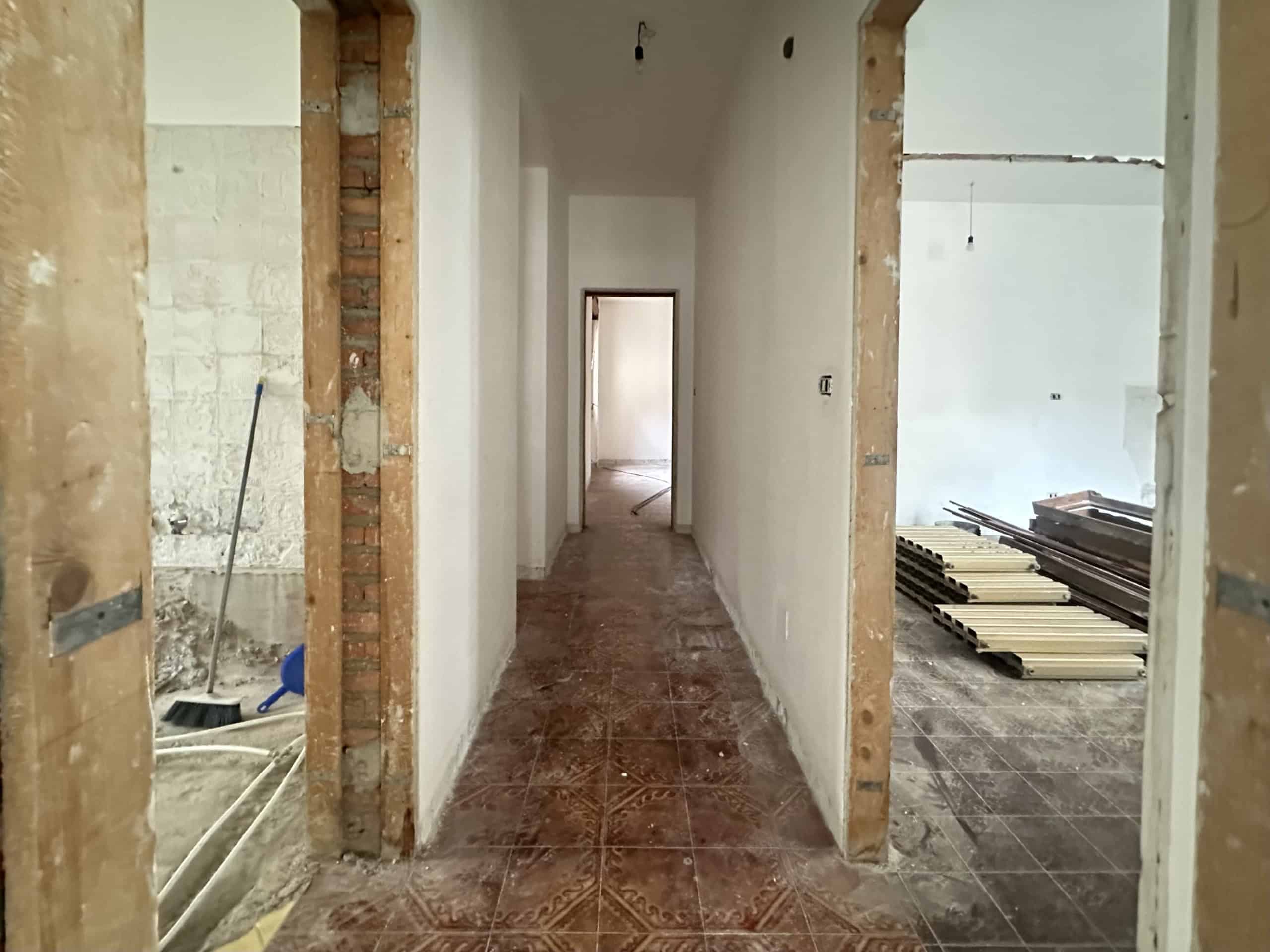 Corpo di corridoio in costruzione con pareti in fase di finitura e pavimento in piastrelle.