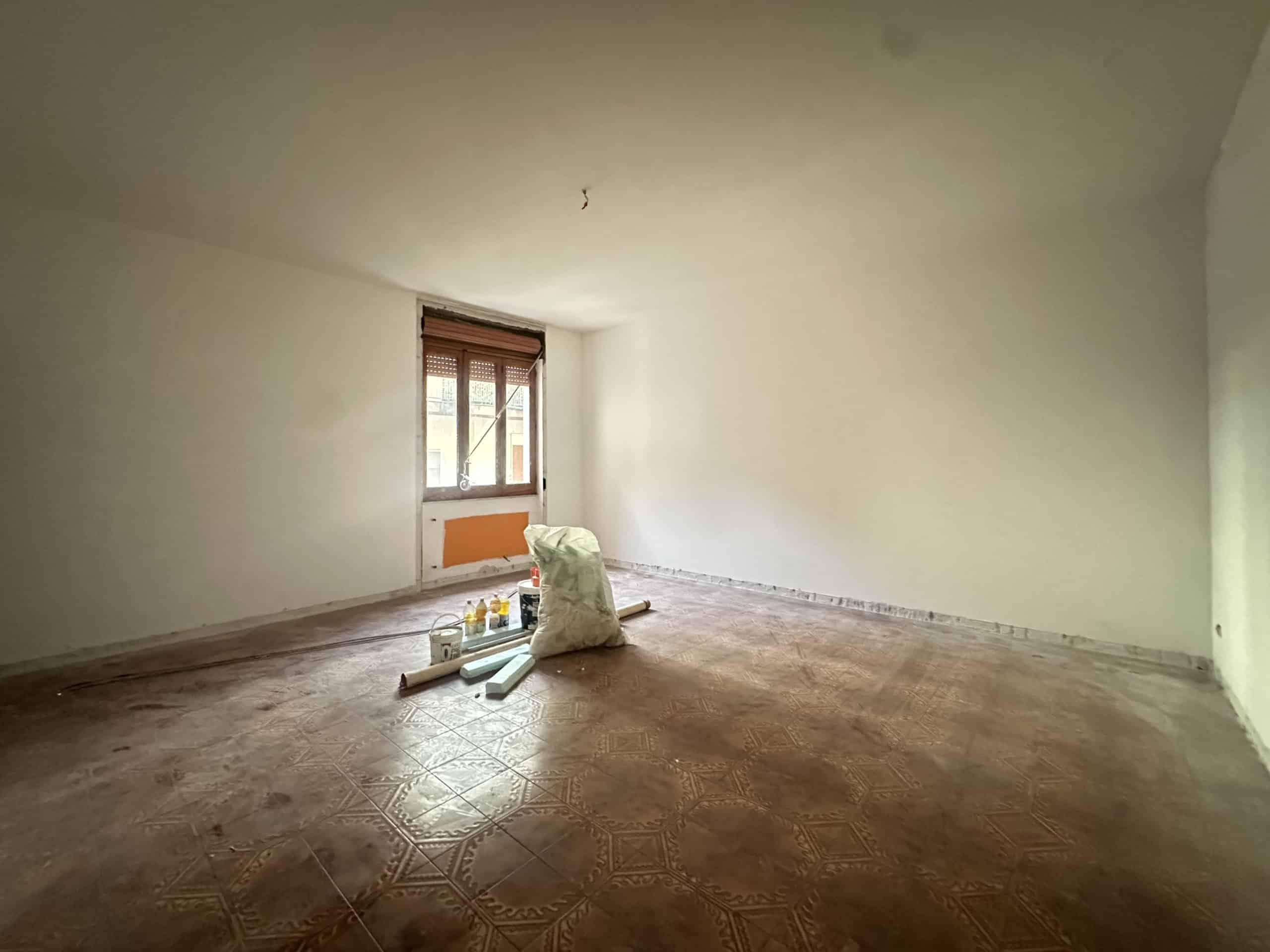 Interno di una stanza vuota in fase di ristrutturazione con pareti bianche e pavimento in piastrelle.