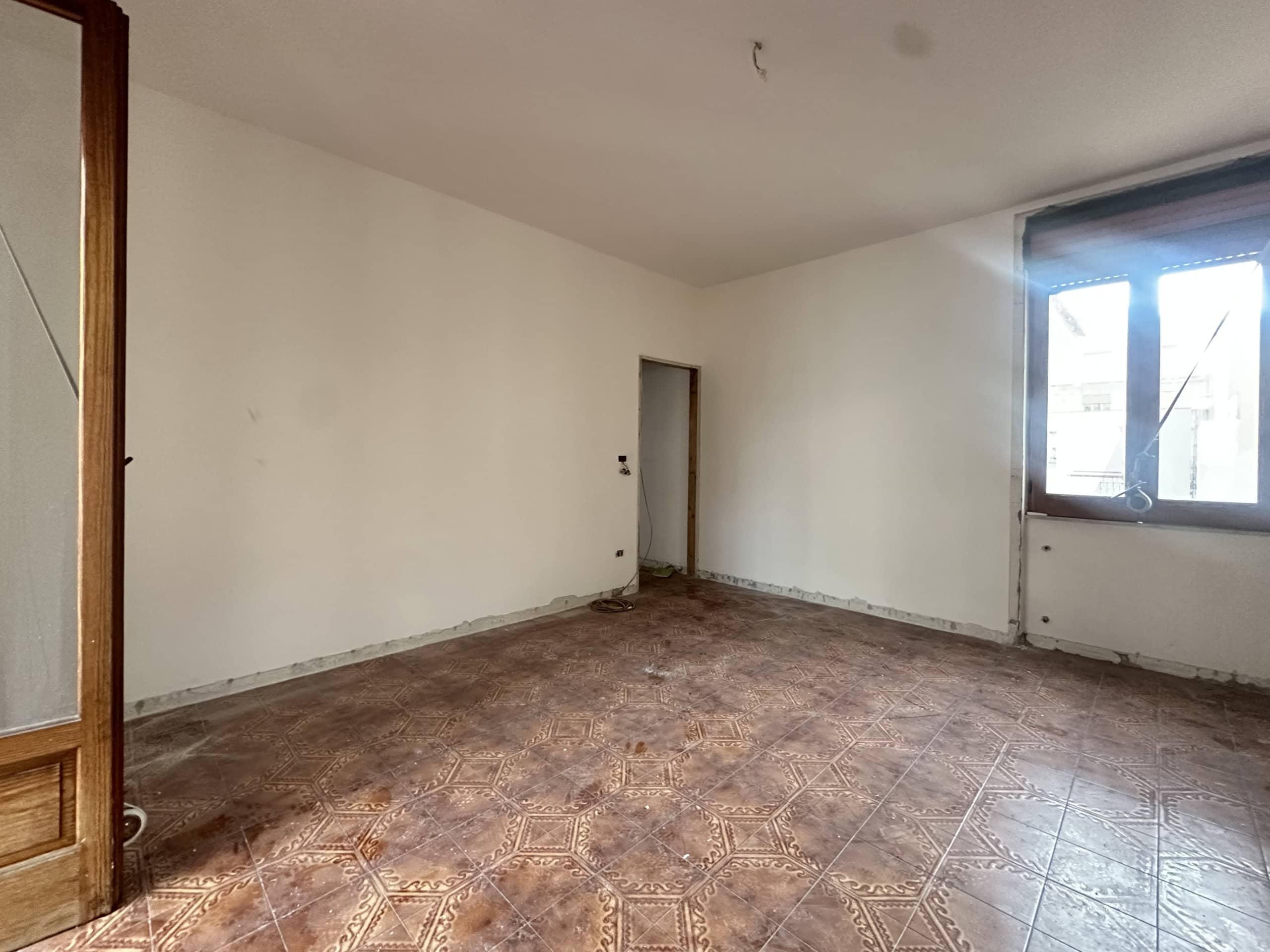 Interno di un appartamento in fase di ristrutturazione con pareti bianche e pavimento in piastrelle decorative, grande finestra che lascia entrare molta luce naturale.