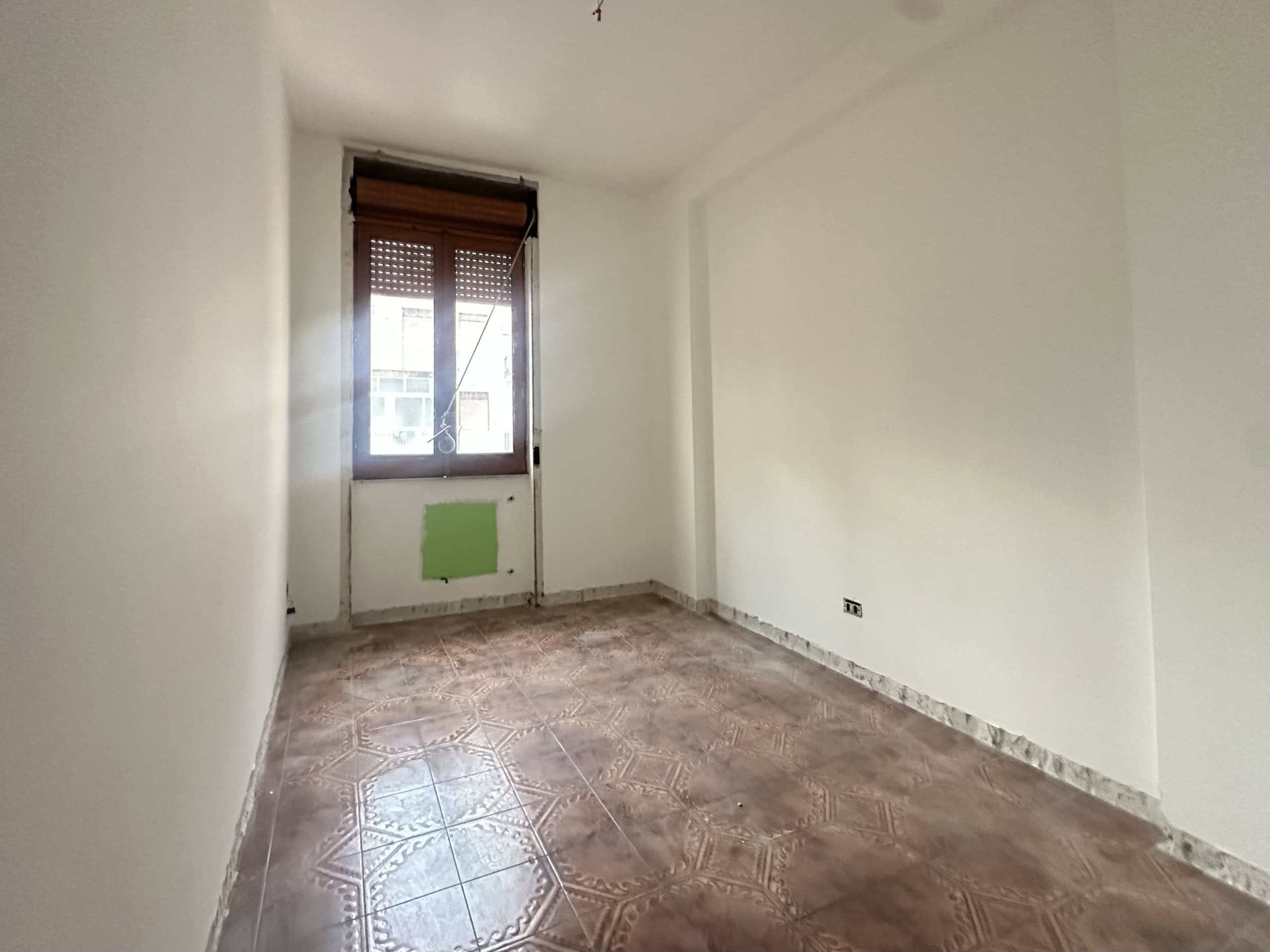 Stanza vuota con pareti bianche, finestra e pavimento in piastrelle, pronta per essere arredato e personalizzato.