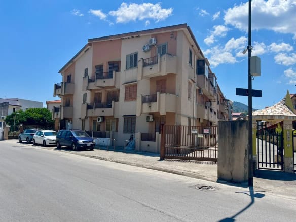 Edificio residenziale a Oliveri con balconi e parcheggio, vicino alla strada principale, sotto un cielo sereno.