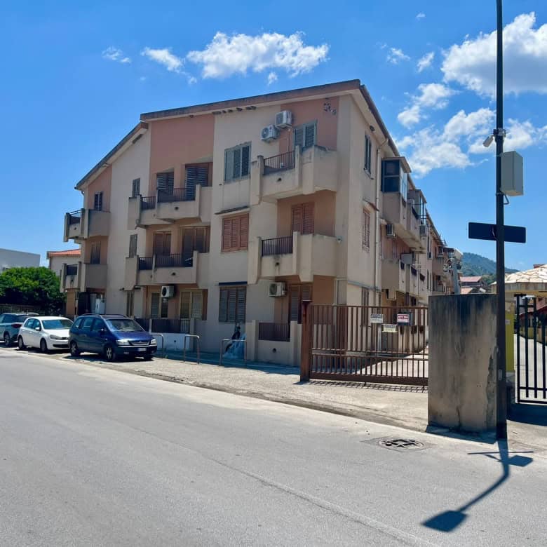 Edificio residenziale a Oliveri con balconi e parcheggio, vicino alla strada principale, sotto un cielo sereno.