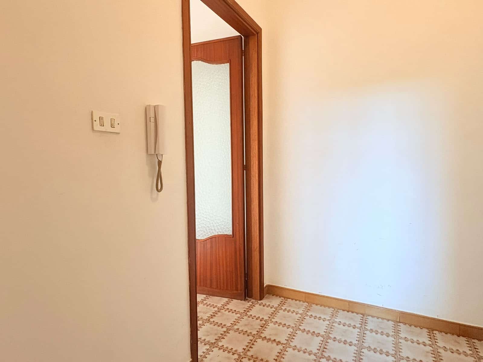 Ingresso di un appartamento in affitto a Milazzo, con porta in legno e pareti bianche.