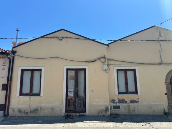 Casa indipendente in vendita a Milazzo, vista frontale con due finestre e porta centrale, pareti gialle e tetto spiovente.