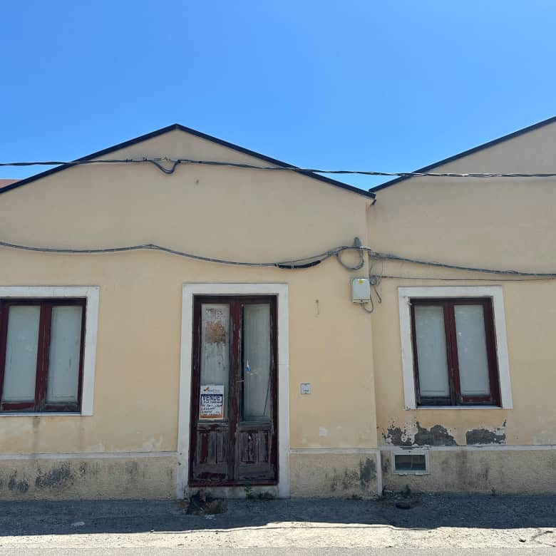 Casa indipendente in vendita a Milazzo, vista frontale con due finestre e porta centrale, pareti gialle e tetto spiovente.