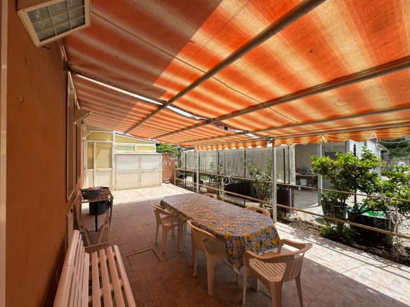Terrazza con tavolo e sedie sotto tenda arancione, vista su giardino e case circostanti.