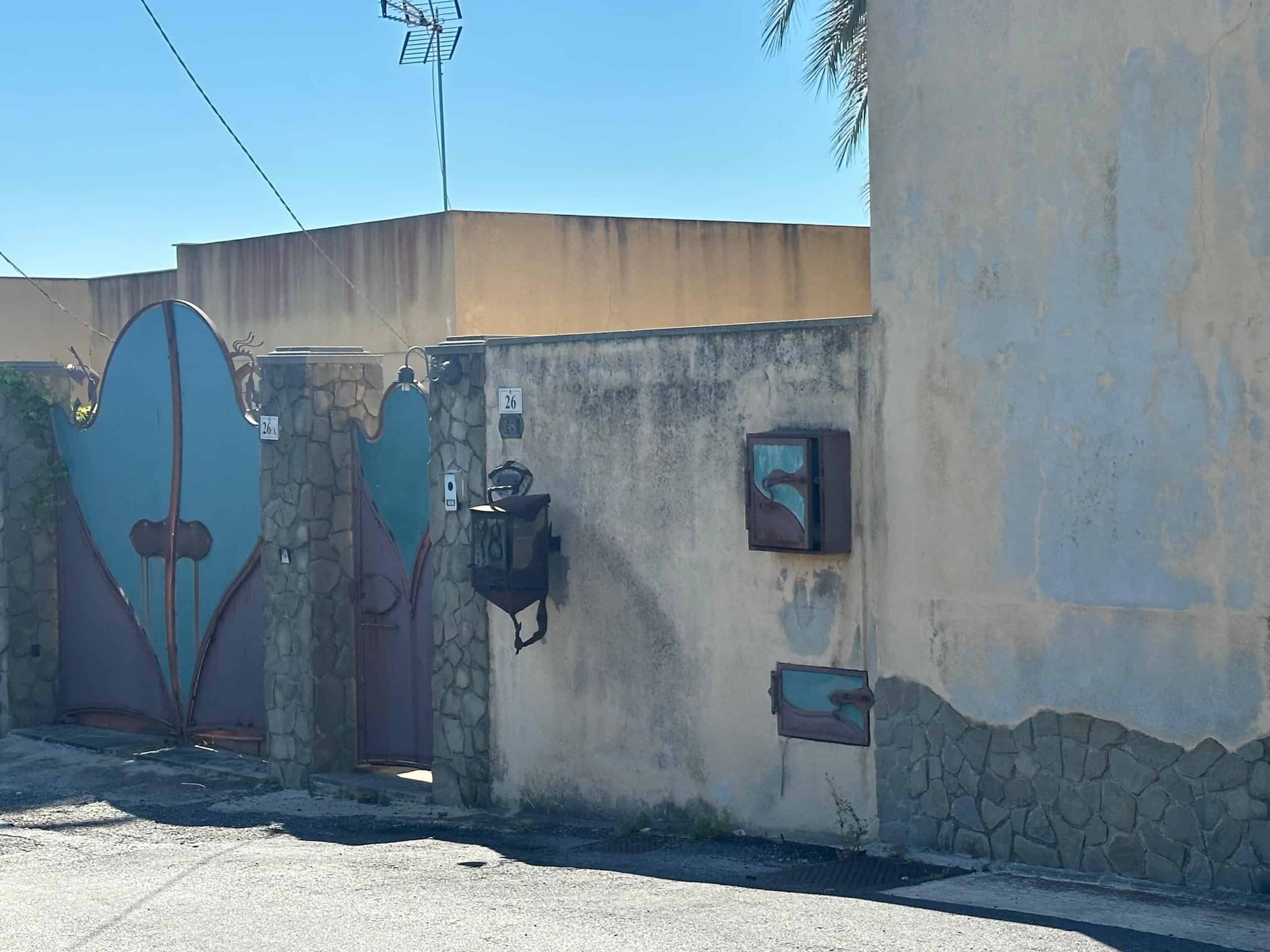 Ingresso di una villa a Milazzo con cancello in ferro battuto e pareti in pietra e cemento.