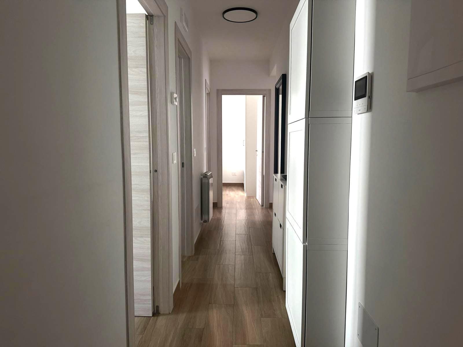 Interno di un appartamento in vendita a Milazzo, corridoio con pavimento in legno e pareti bianche.