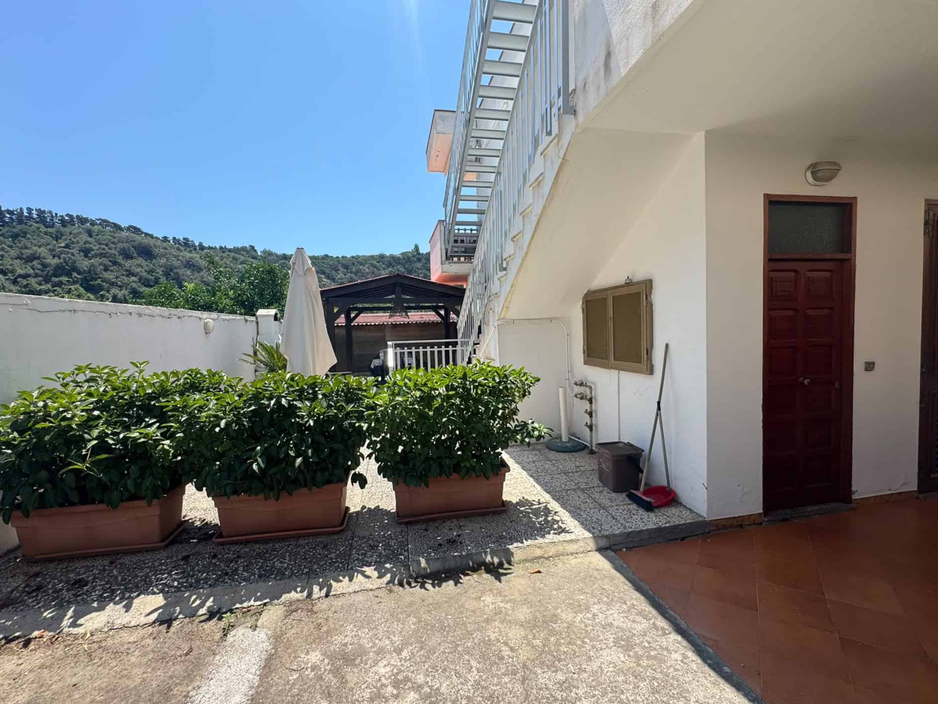 Balcone e ingresso di una villa in vendita a Milazzo con piante in vaso e vista sul verde circostante.