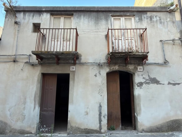 Facciata di un edificio storico con due balconi in ferro battuto e porte in legno, in condizioni di deterioramento, situato in un contesto urbano.