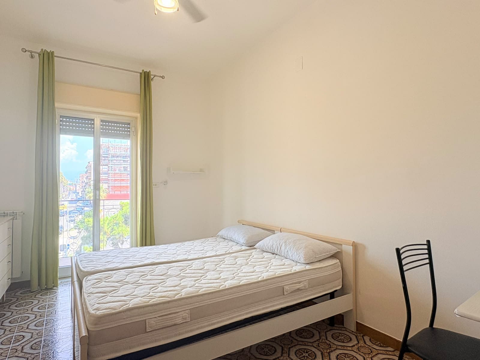 Camera rivolta verso un letto matrimoniale in una stanza luminosa con finestra e tende verdi.