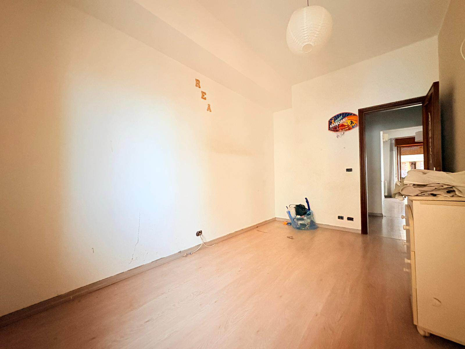Interno di un appartamento in affitto a Milazzo, con pareti bianche e pavimento in legno chiaro, decorato con lettere sulla parete e oggetti vari.