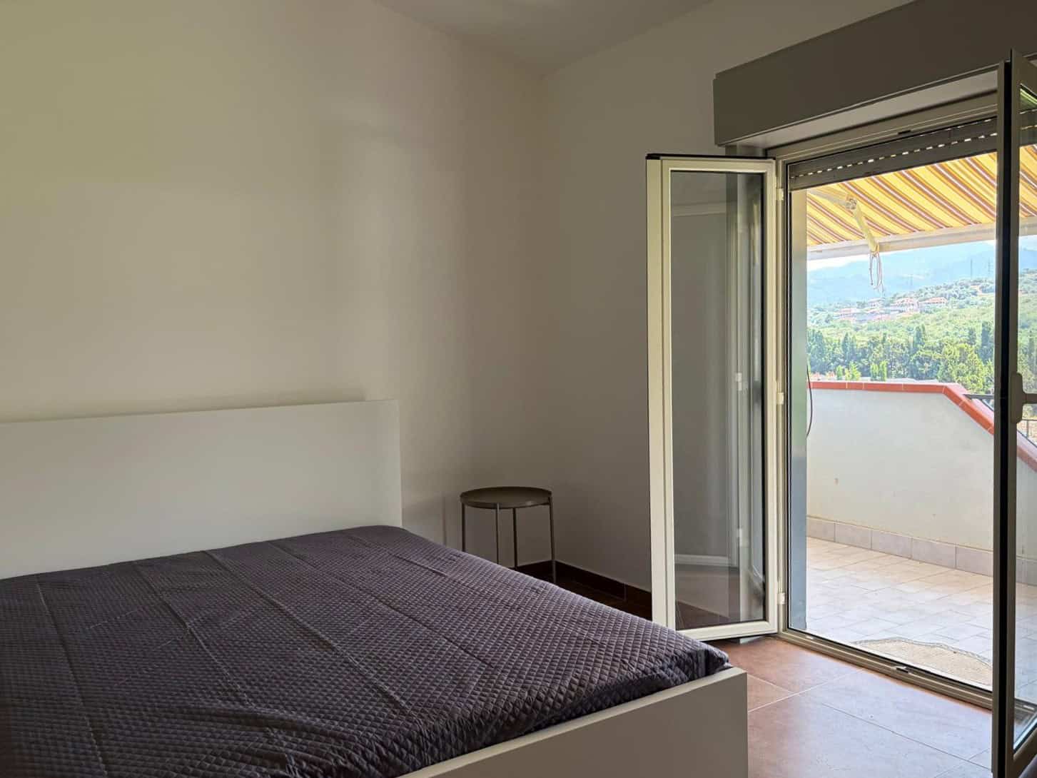 Camera che mostra una camera da letto luminosa con balcone e vista panoramica sulla natura circostante.