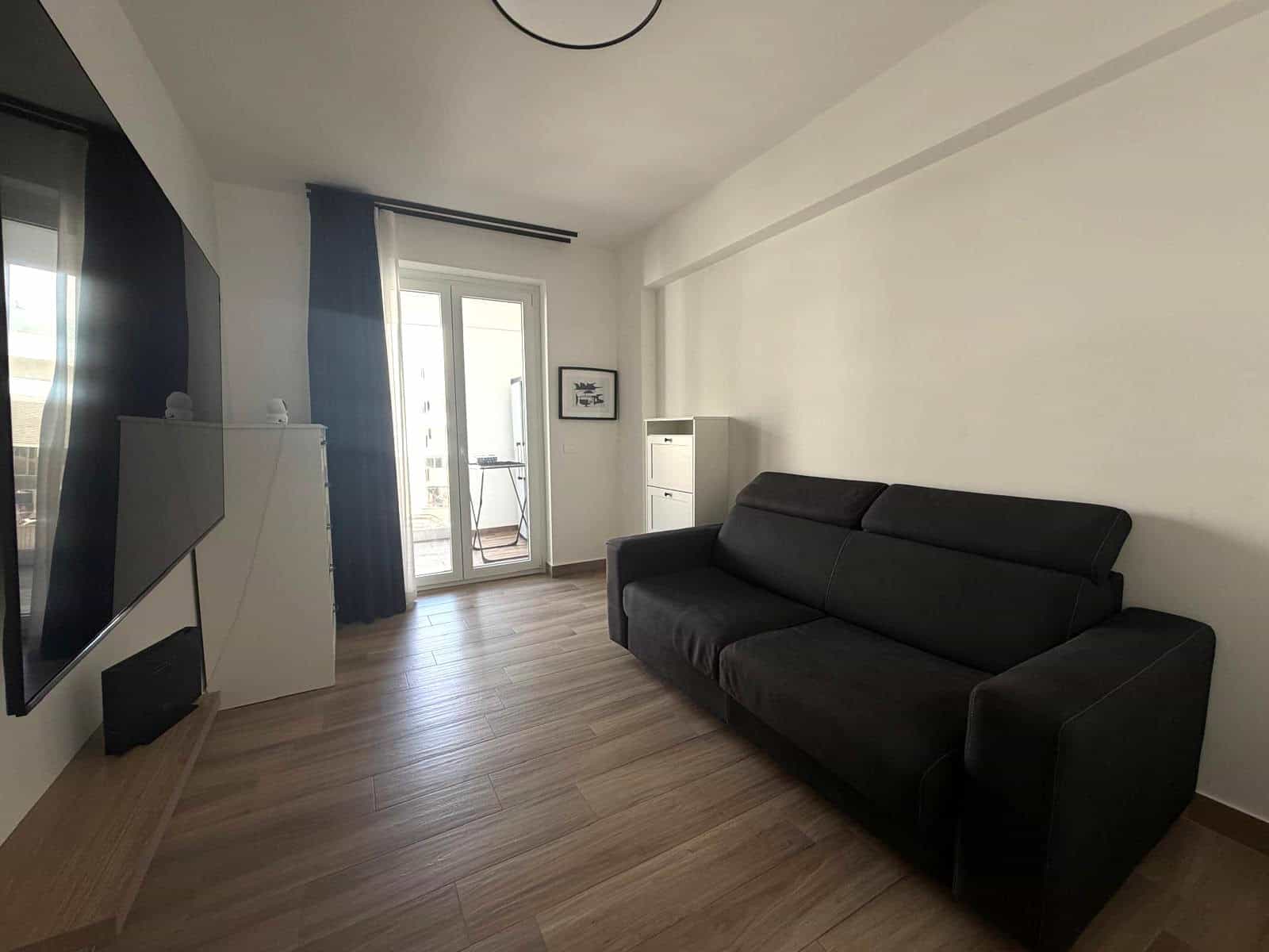 Interno di un appartamento in vendita a Milazzo, soggiorno con divano nero e accesso a balcone con vista.