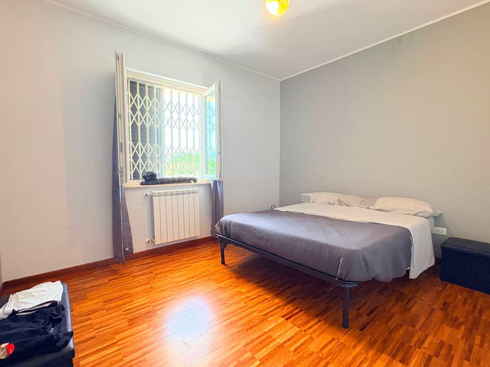 Camera da letto spaziosa con pareti bianche, pavimento in legno e finestra con grate e tende.