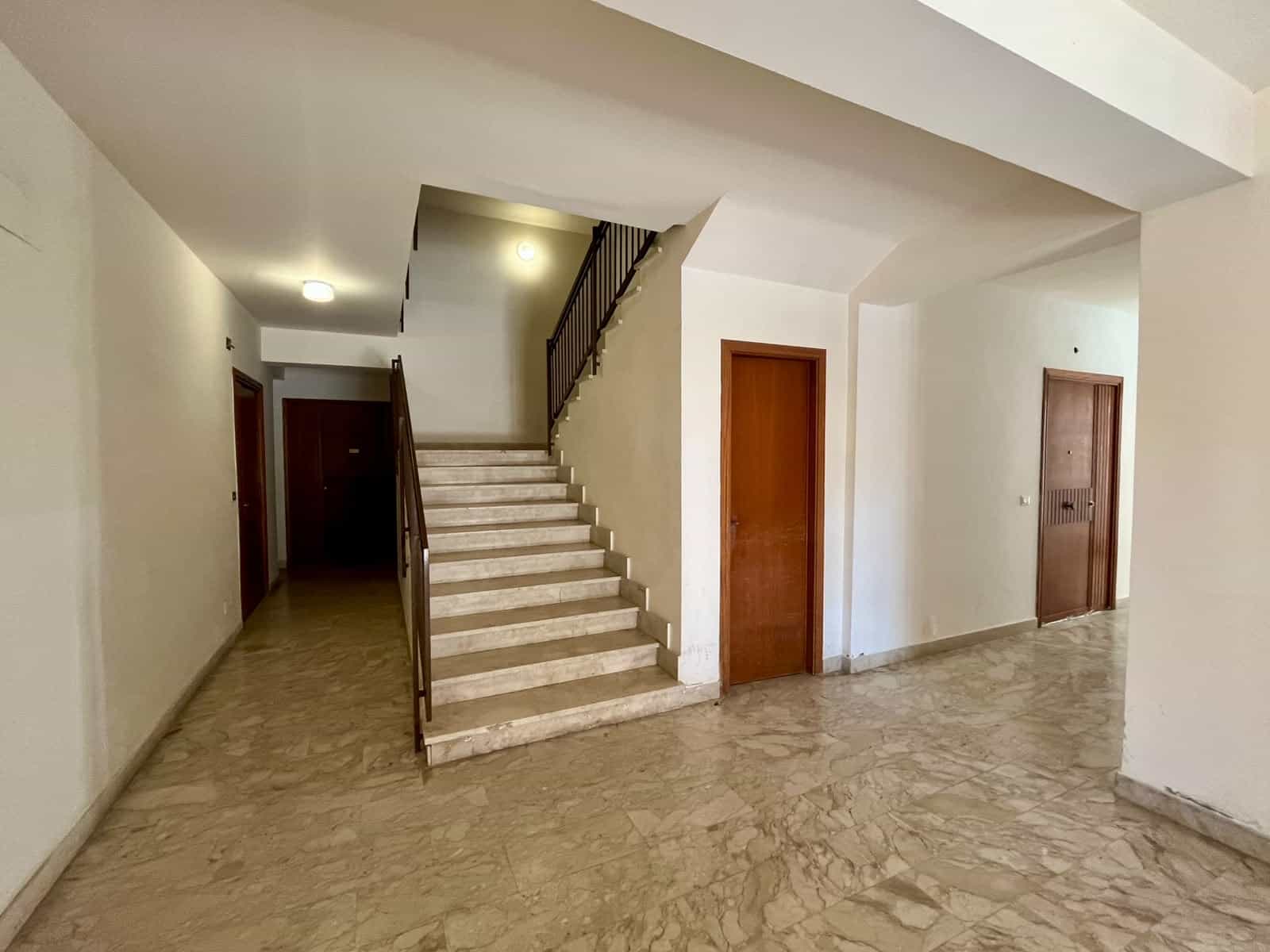 Interno di un appartamento con scala in marmo e pareti bianche, zona soggiorno luminosa e spaziosa.