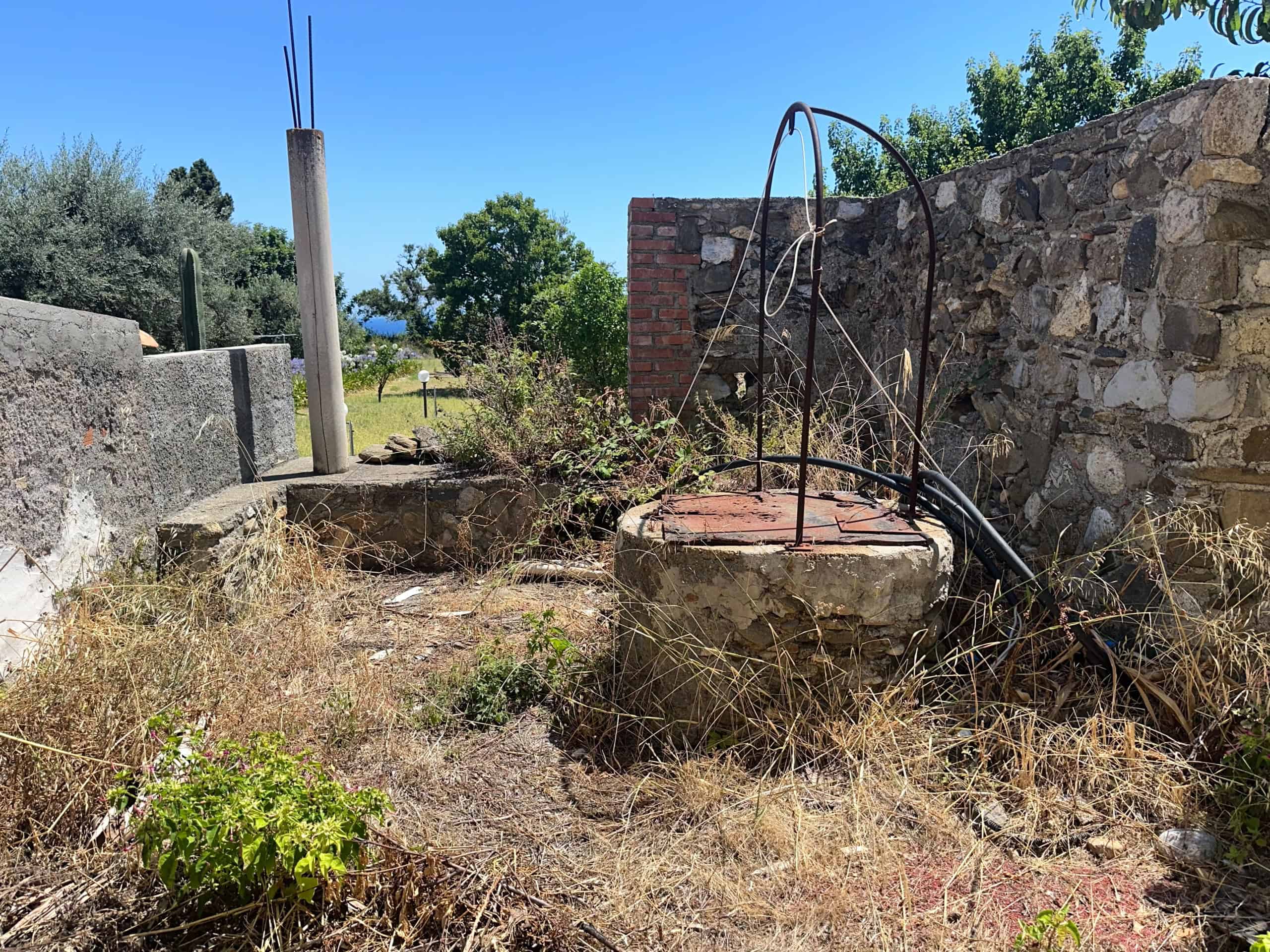 Antico pozzo abbandonato in un cortile rustico con muri in pietra e vegetazione selvaggia.