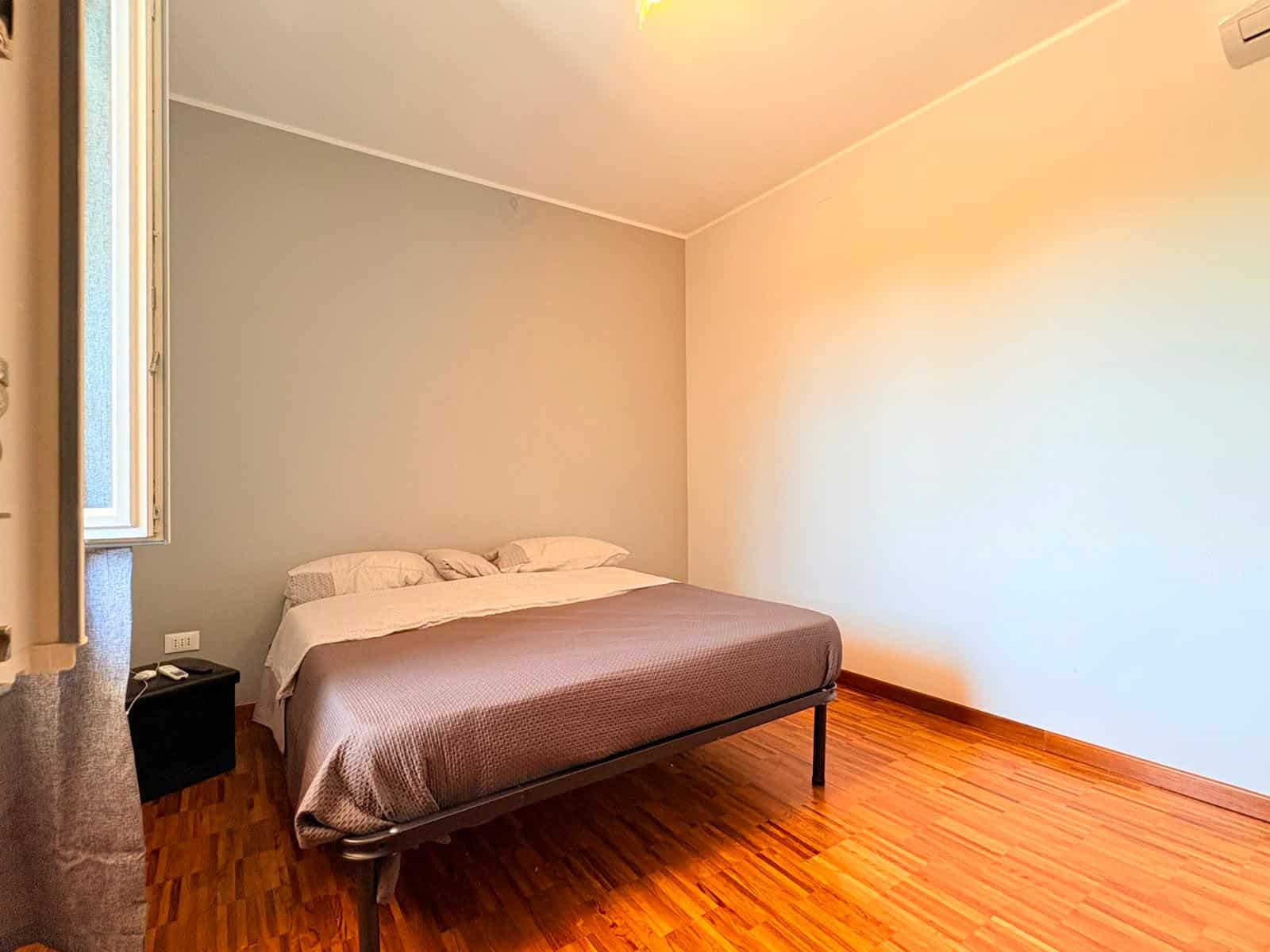 Camera da letto moderna con pareti neutre e pavimento in legno, letto matrimoniale e finestra luminosa.