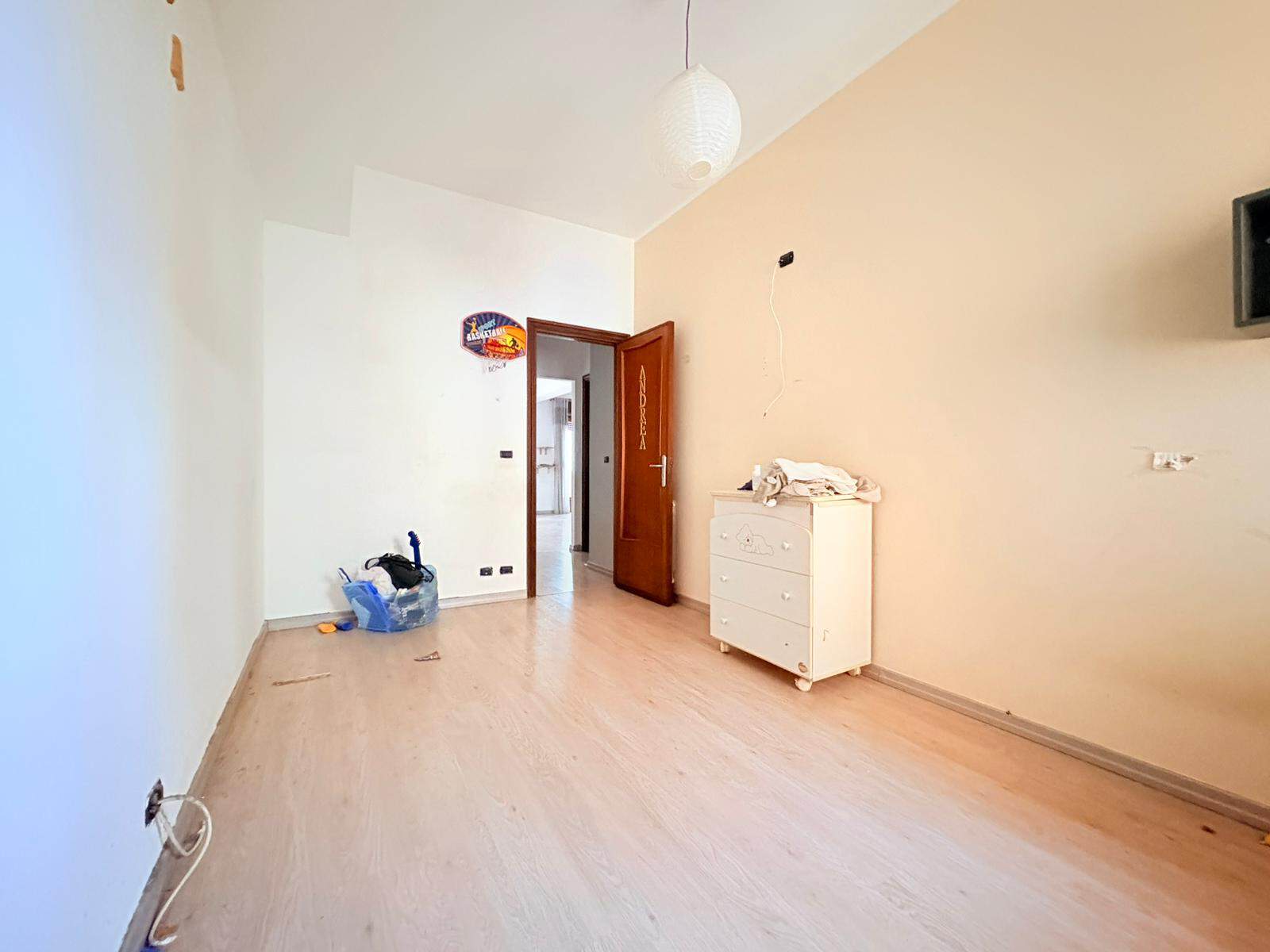 Interno di un appartamento in affitto a Milazzo, stanza luminosa con pareti bianche e arancioni, pavimento in legno chiaro, mobili essenziali e decorazioni minimaliste.