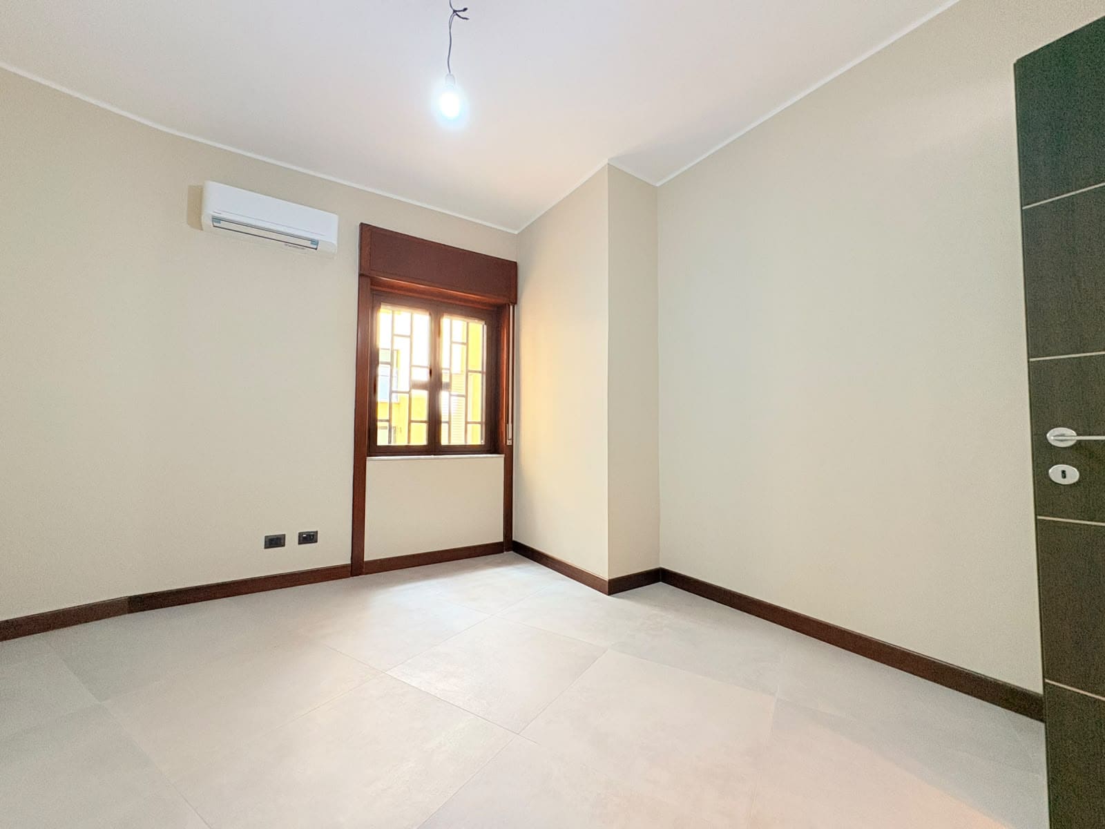 Interno di un appartamento in vendita a Milazzo, con pareti beige, finestra con infissi in legno e aria condizionata.