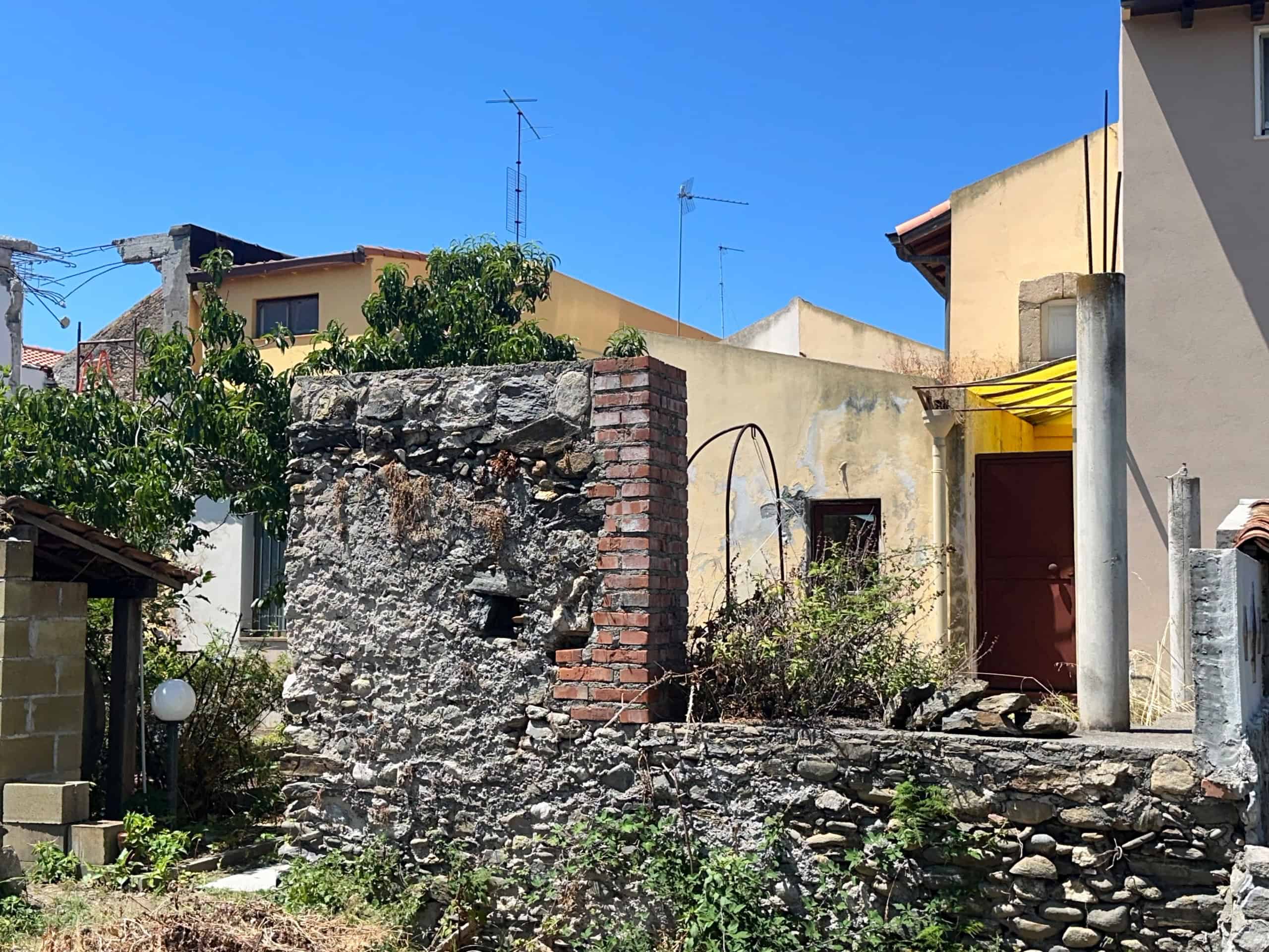 Vista esterna di una proprietà immobiliare a Milazzo con muro in pietra e piante verdi sotto un cielo azzurro.