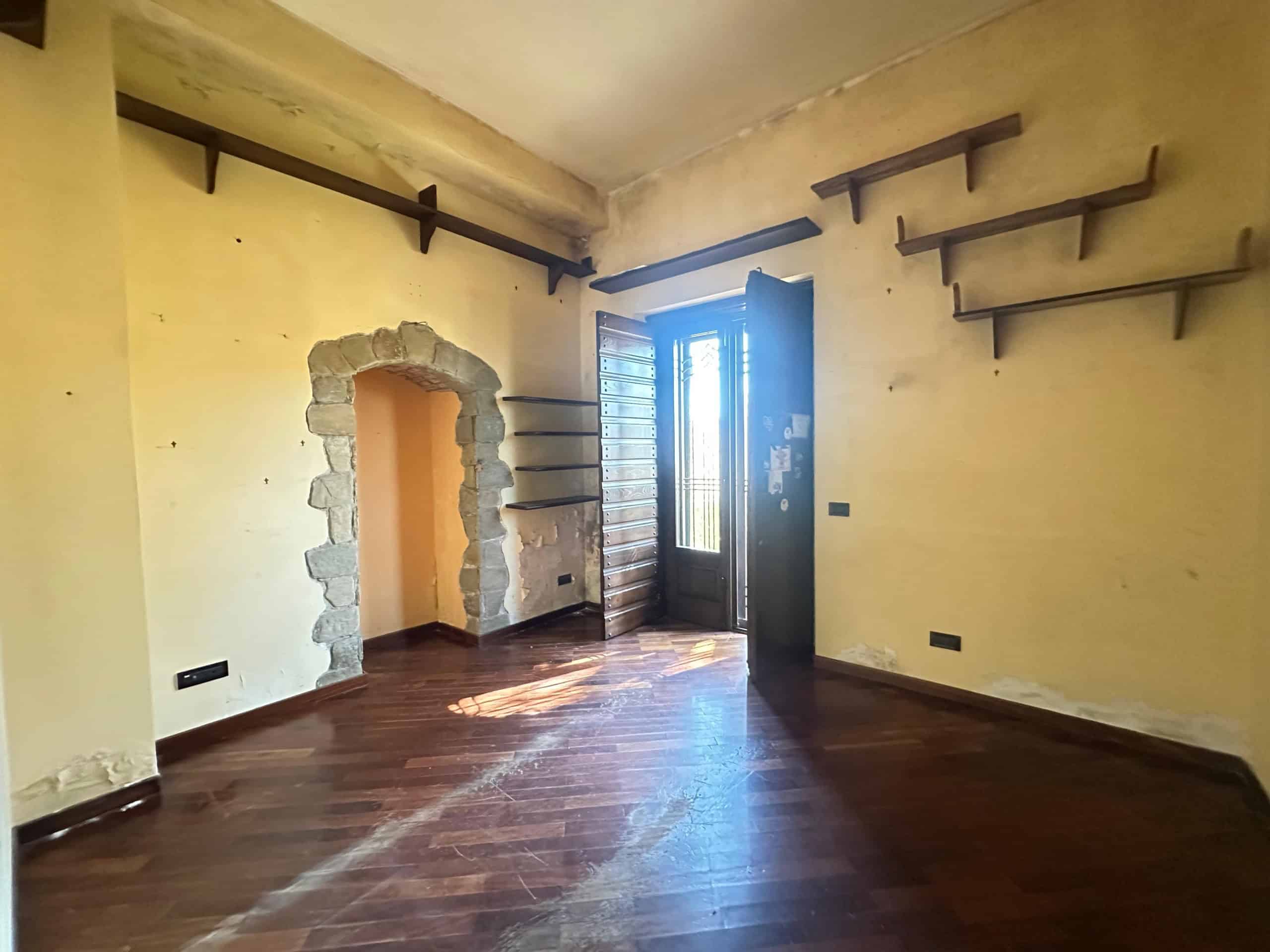 Interno di una villa in vendita a Milazzo con pareti gialle, scaffali in legno e porta finestra che dà sul balcone.