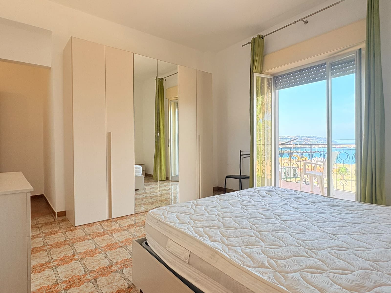 Camera che mostra una camera da letto luminosa con vista mare, armadio a specchio e balcone con vista panoramica.