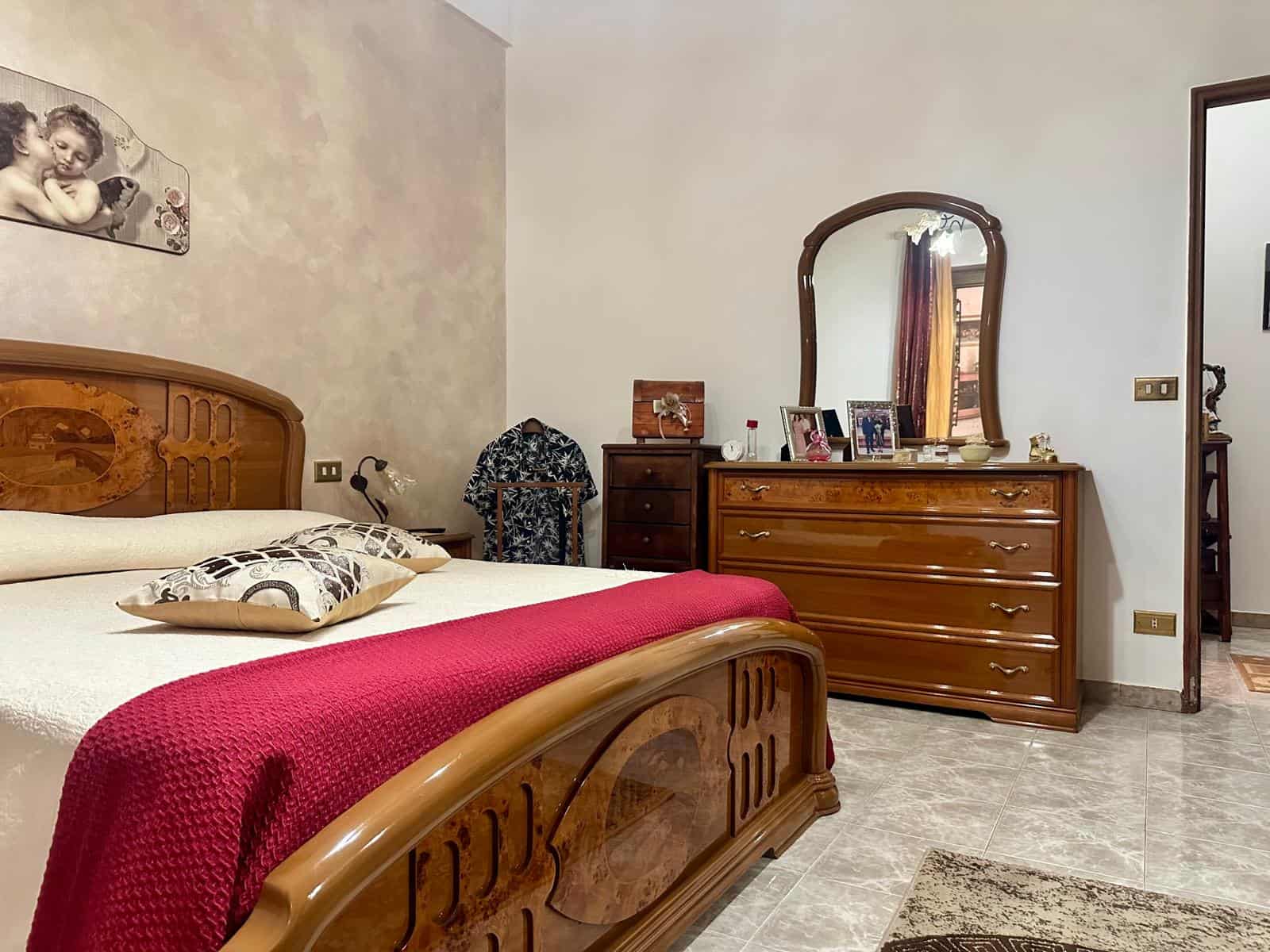 Camera da letto con letto in legno, coperta rossa e armadio con specchio, arredamento classico in stile tradizionale.