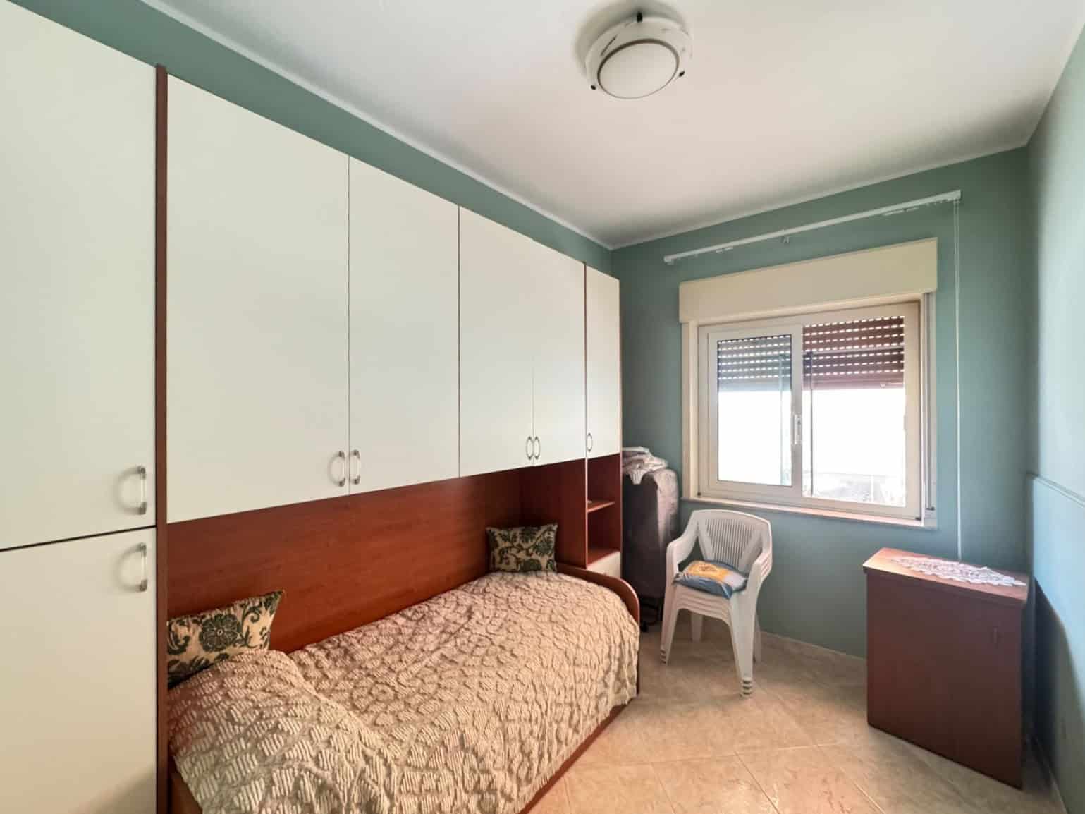 Camera mostra una stanza con letto singolo, armadio a muro e finestra con persiana, in un appartamento in vendita a Oliveri.