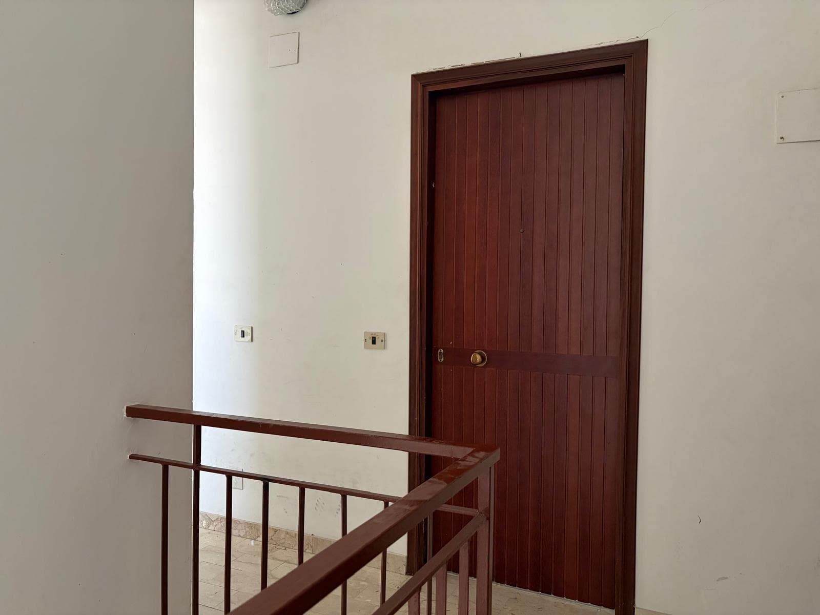 Porta in legno scuro in un appartamento in affitto a Falcone, Me, con ringhiera in metallo e pareti bianche.