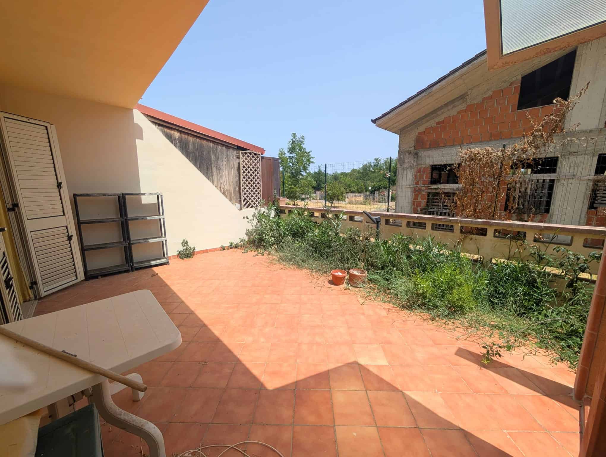 Terrazza di villetta a schiera con piante e vista su costruzioni vicine, pavimentata in piastrelle arancioni.