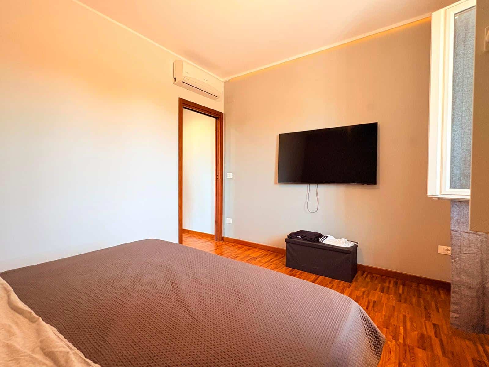 Camera da letto moderna con pareti beige, TV a schermo piatto e pavimento in legno, in un appartamento in vendita a Milazzo.