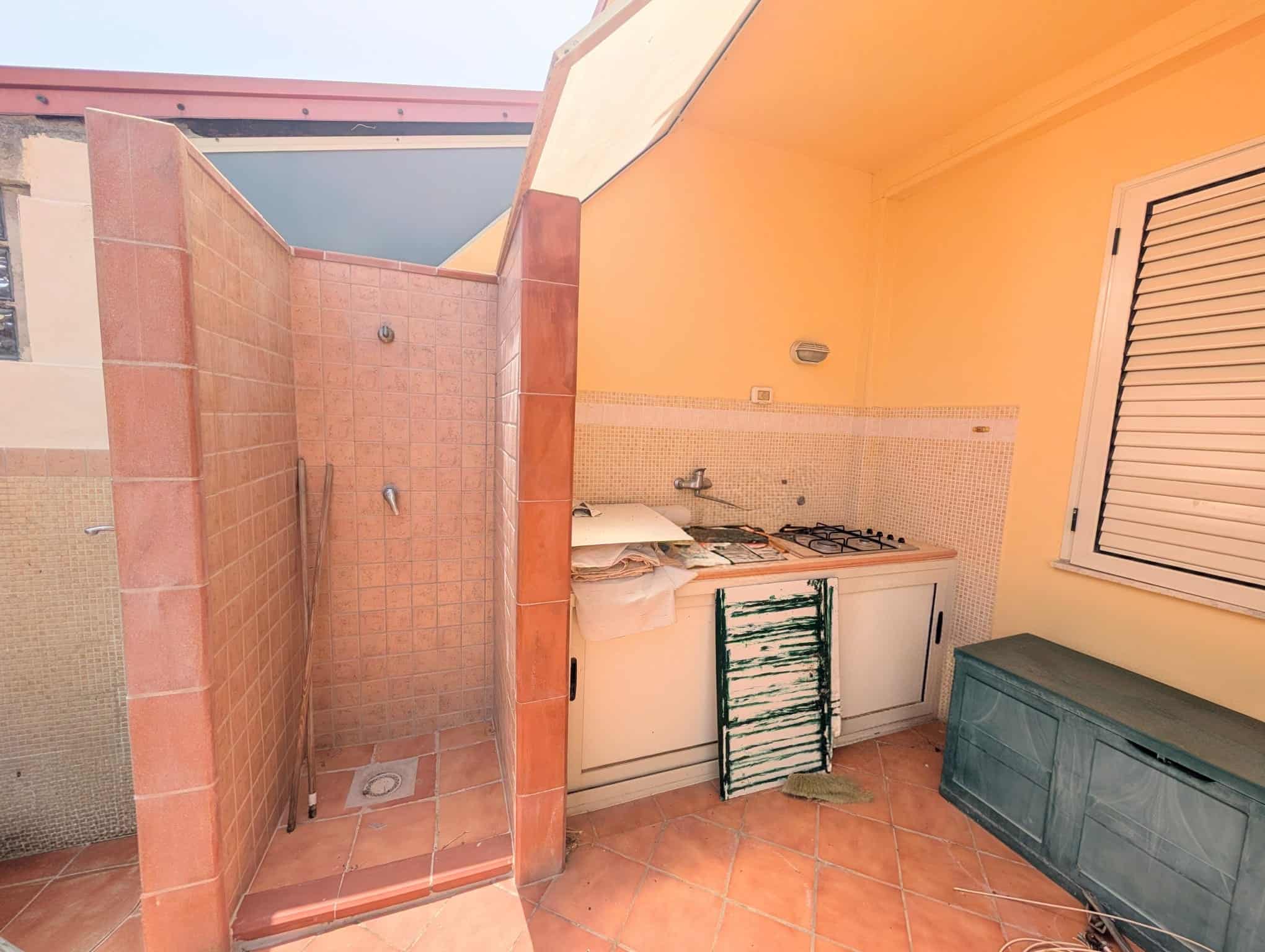 Zona esterna con doccia e cucina all'aperto in una villetta a schiera, con pareti in mattoni e pavimento in piastrelle.