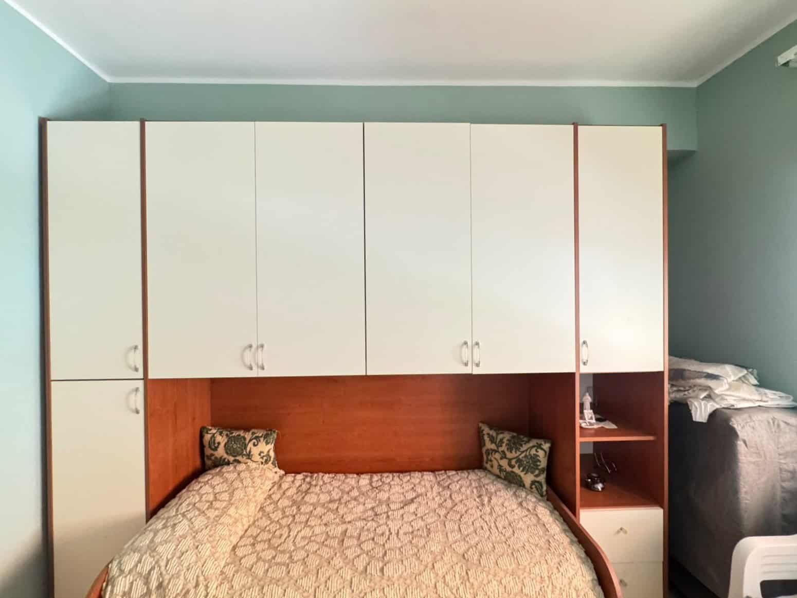 Camera da letto con armadio a muro bianco e letto matrimoniale con cuscini decorativi.