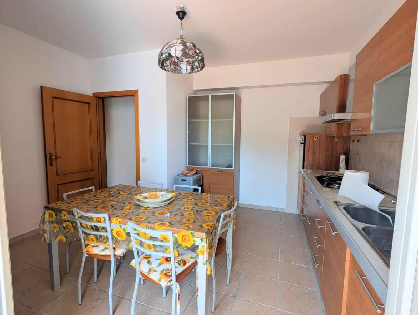 Cucina moderna con tavolo da pranzo, sedie e mobili in legno, ambiente luminoso e accogliente.